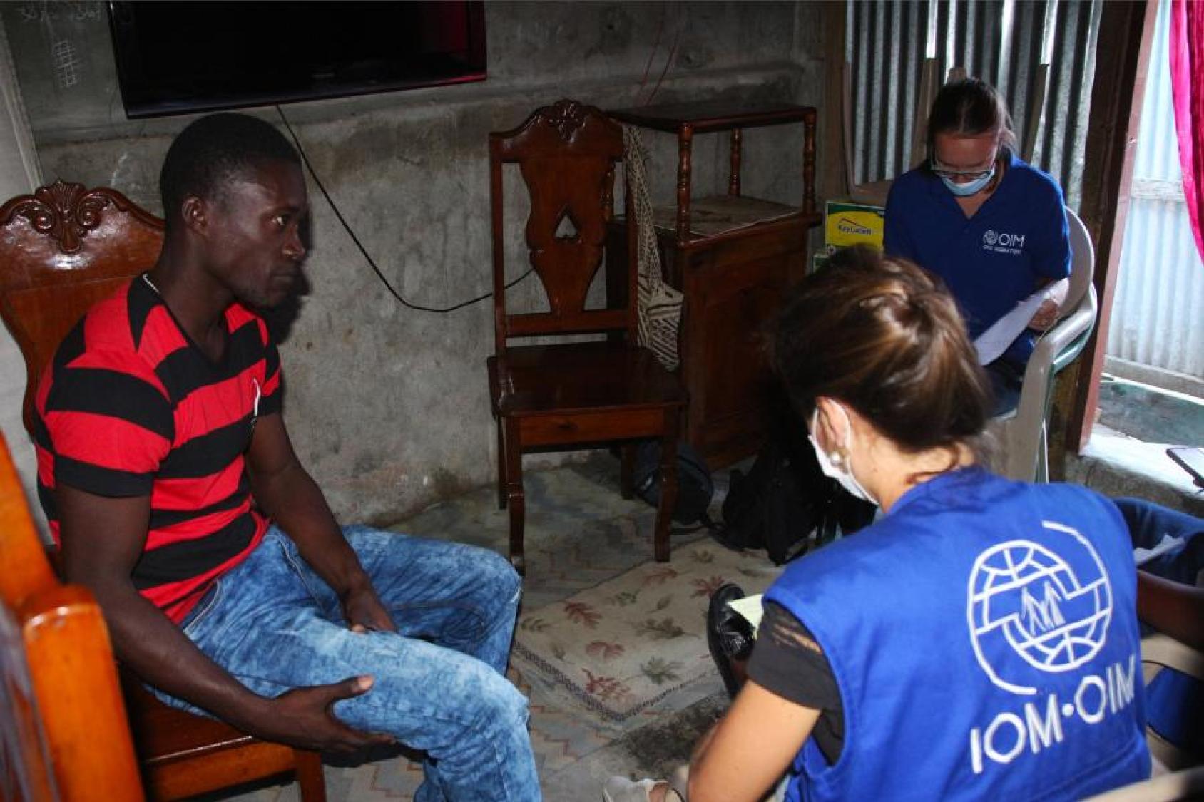 IOM staff sit in a living room with a gentleman. 