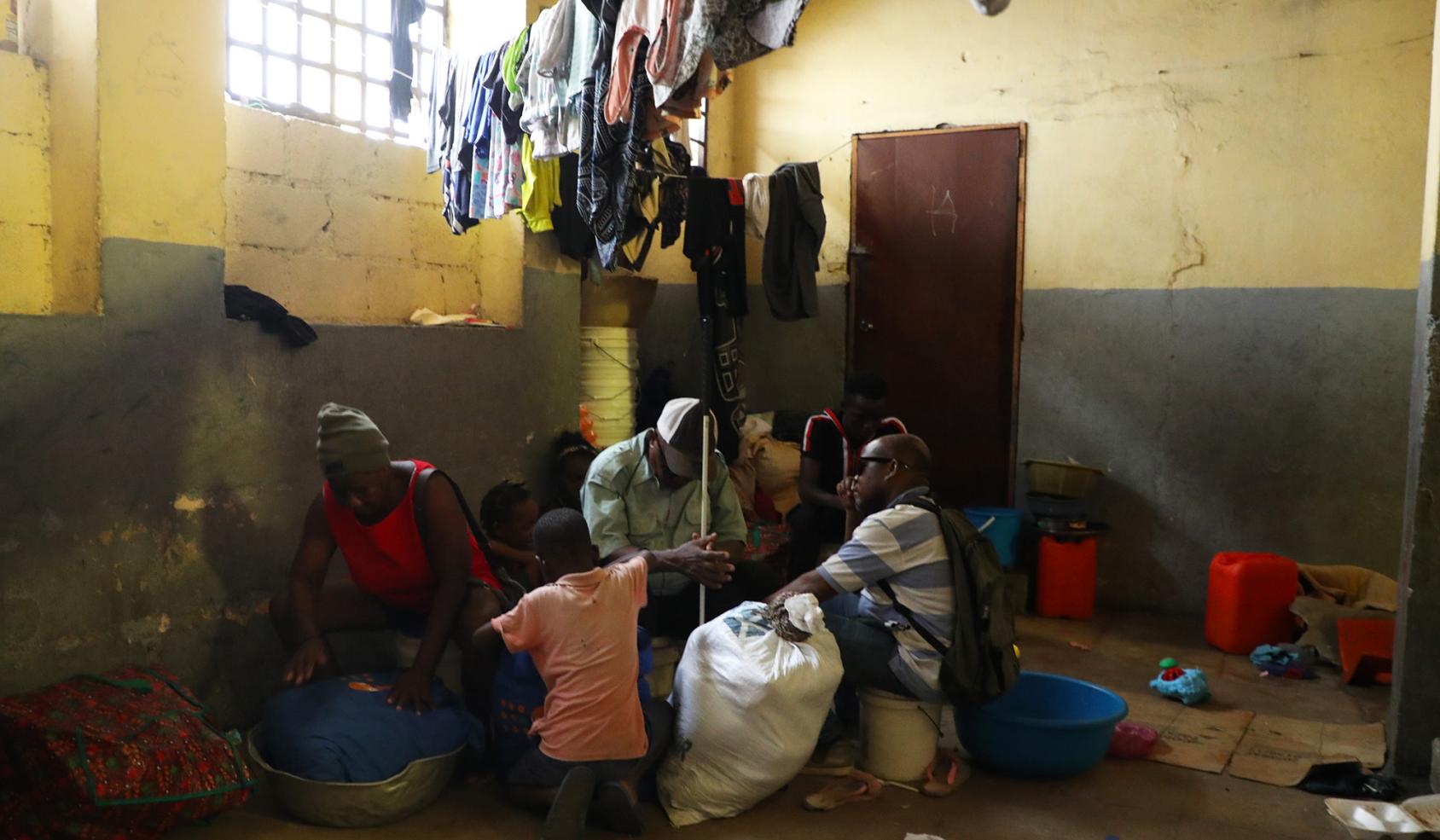 Three men, a woman and two children sit together underneath clothing lines of washed, hanging clothes.