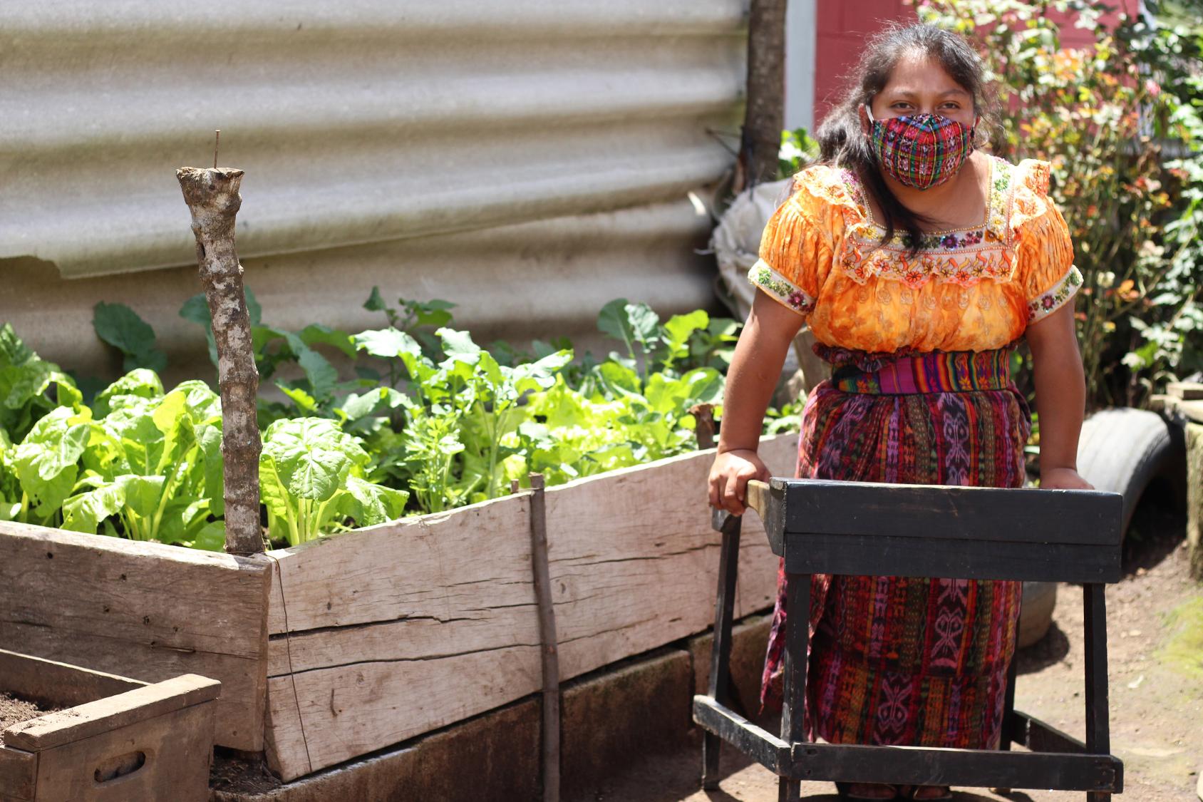An indigenous woman with a physical disability stands by a bed of vegetation. 
