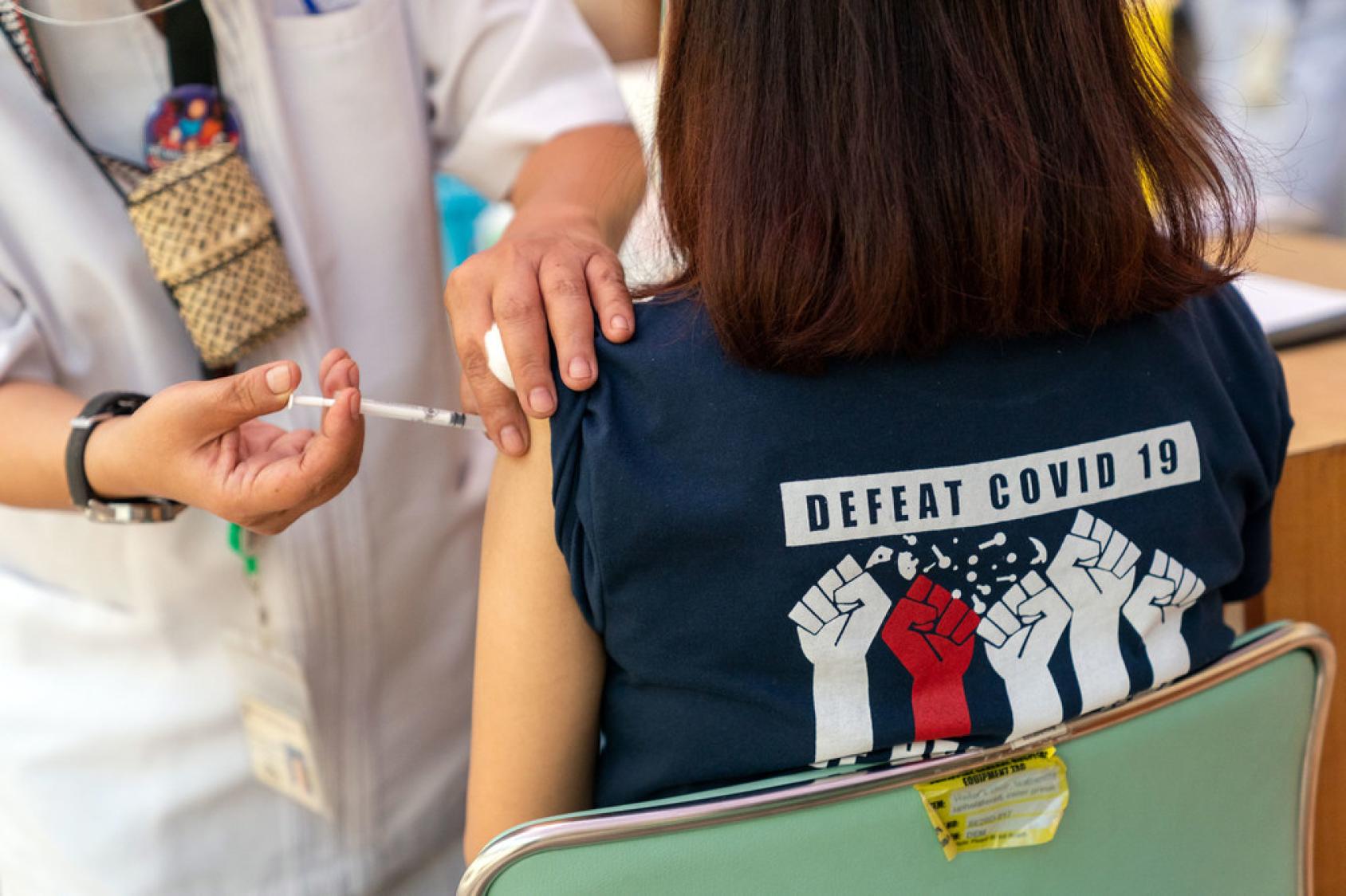 Una chica con una camiseta con el mensaje "Derrotar el COVID-19" en inglés, recibe la vacuna contra el COVID-19.