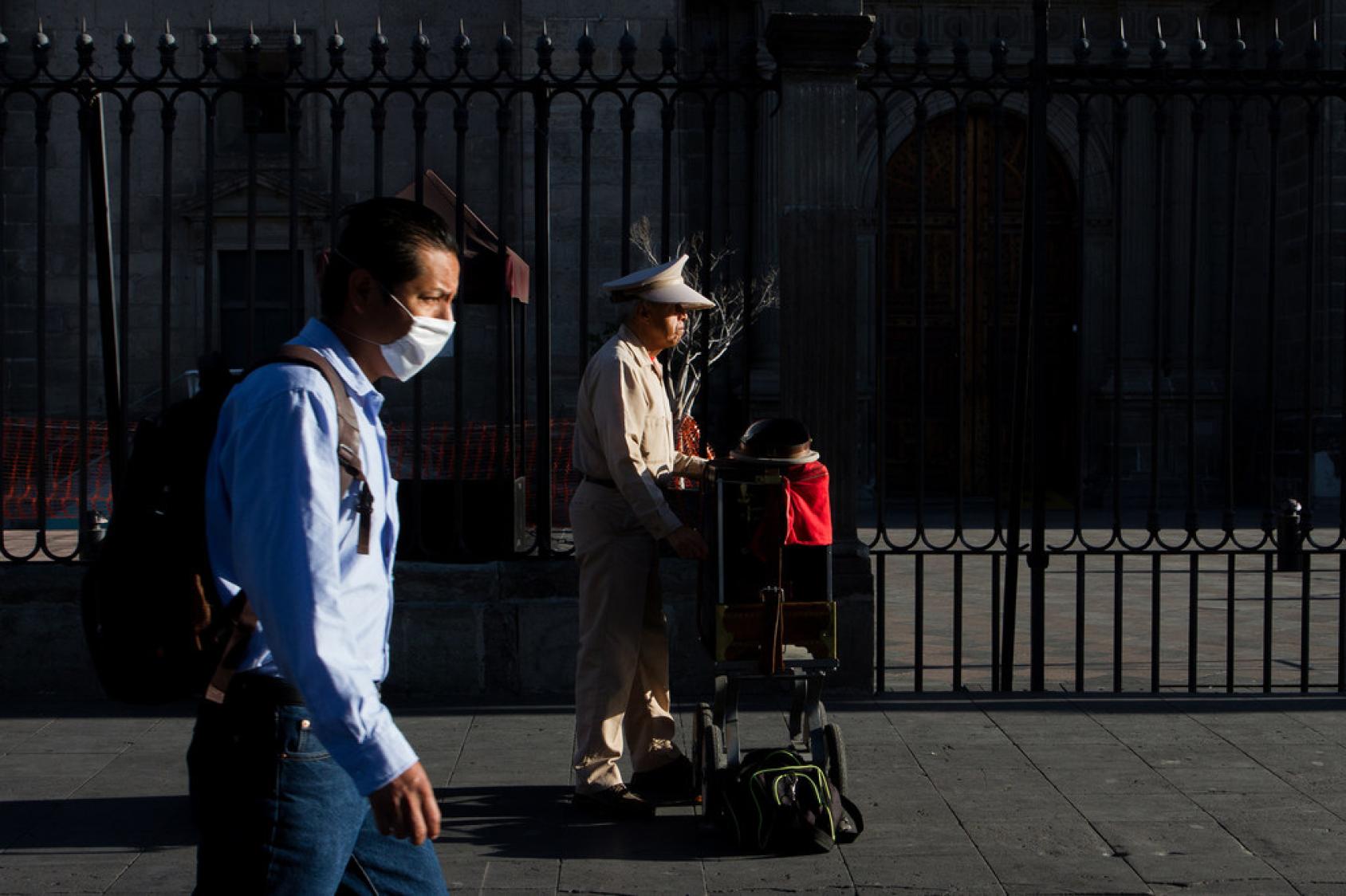 Con una fachada de piedra y una reja negra de fondo, dos hombres caminan sobre la acera, en Ciudad de México.