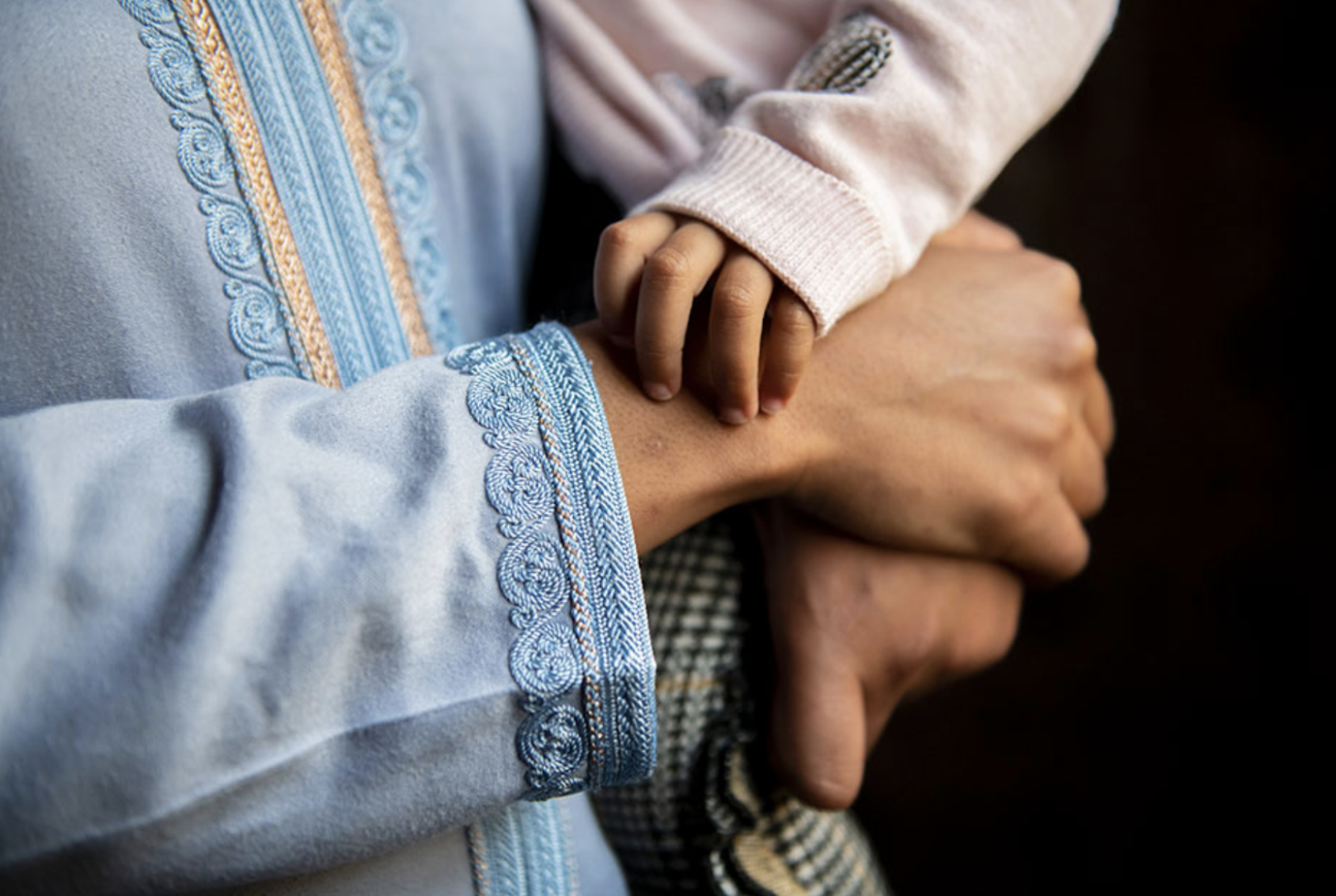 A close up image of hands, in which a man holds up his baby girl.
