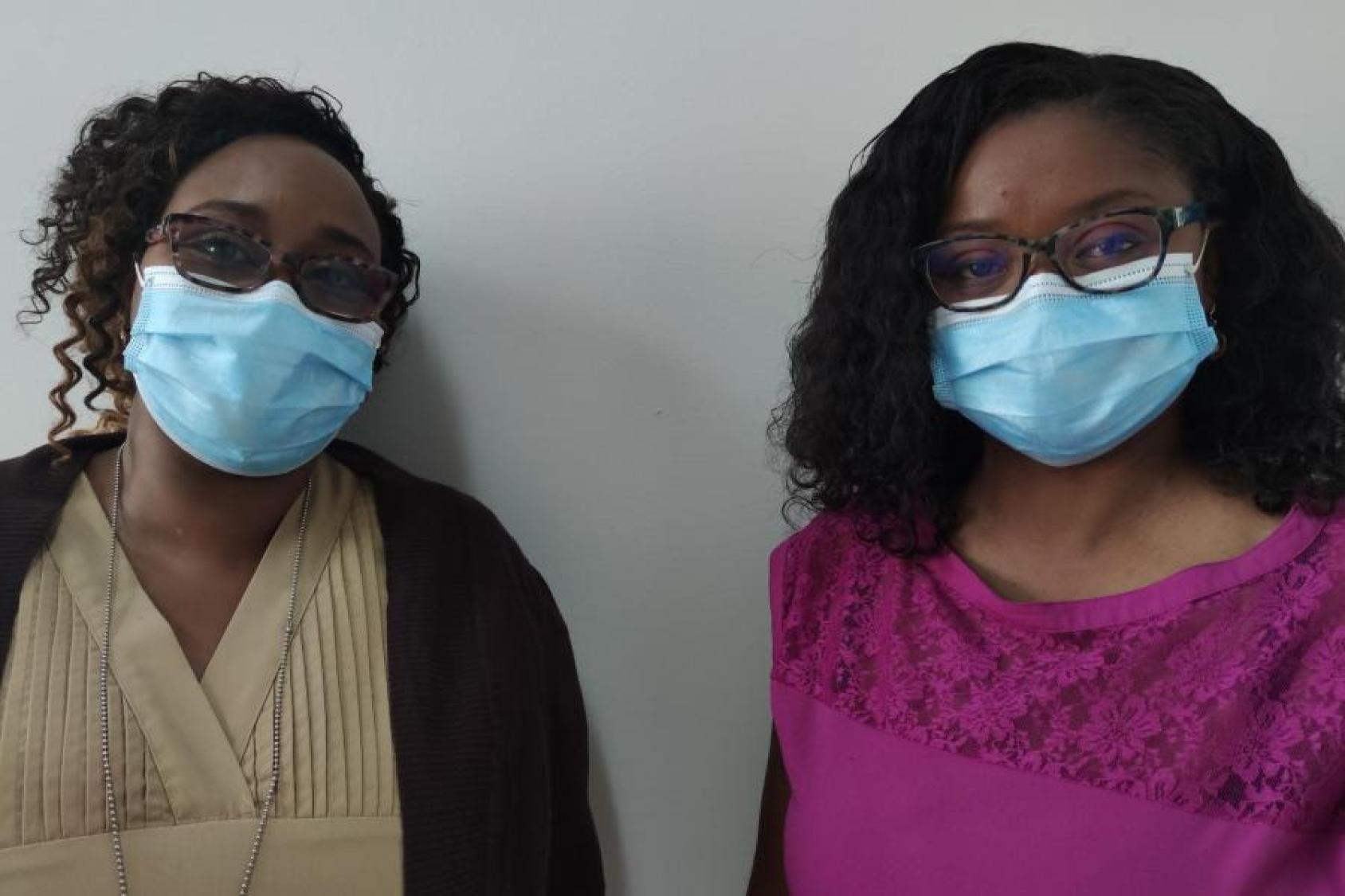 Two women in blue face-masks stand side by side.