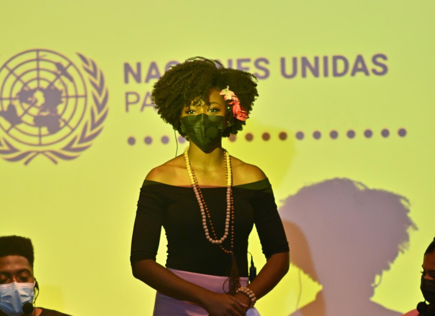 Женщина в маске на лице стоит перед логотипом Организации Объединенных Наций в Панаме. 