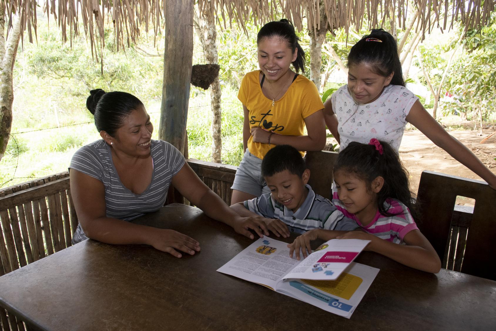 A mother and her children smile as they work together on school assignments. 