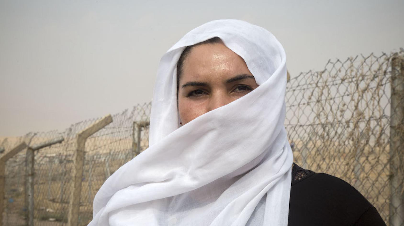 A powerful image of a woman's eyes behind a white scarf near a metal fence. 