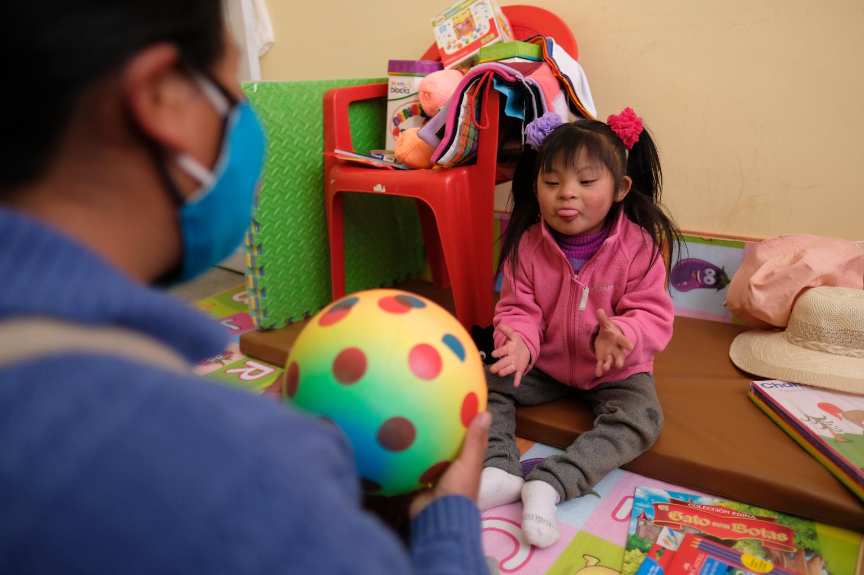 A little girl playing with a a ball and a woman in a blue sweater. 
