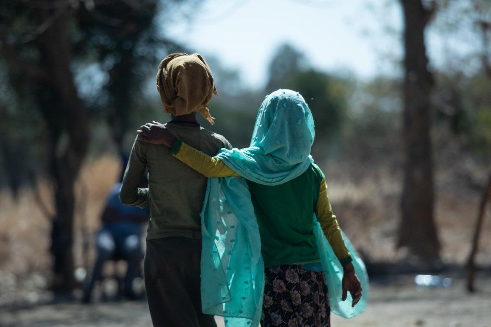Two girls wearing headscarves from Ethiopia are photographed from behind walking down the street, one with her arm around the other's shoulder.