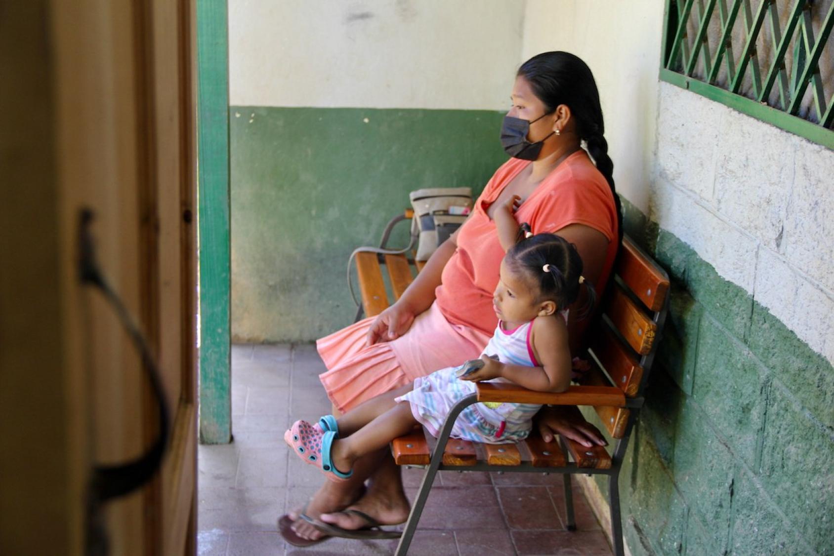 Una mujer y una niña se sientan en un banco mientras esperan su turno en un puesto de salud en La Palma, Costa Rica.