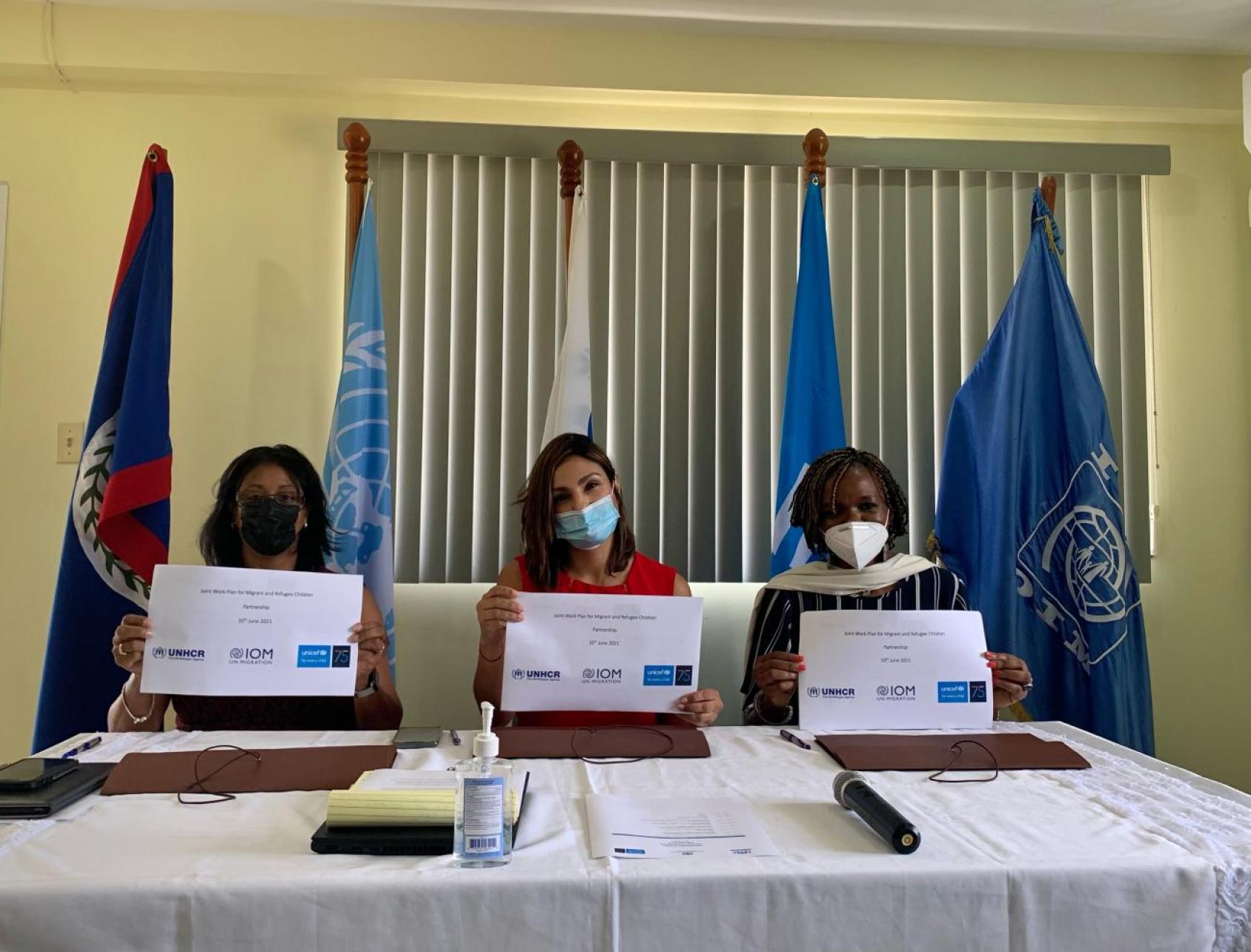 Trois femmes portant chacune un masque de protection respiratoire sont assises à une table et montrent face caméra les documents qu’elles viennent de signer.
