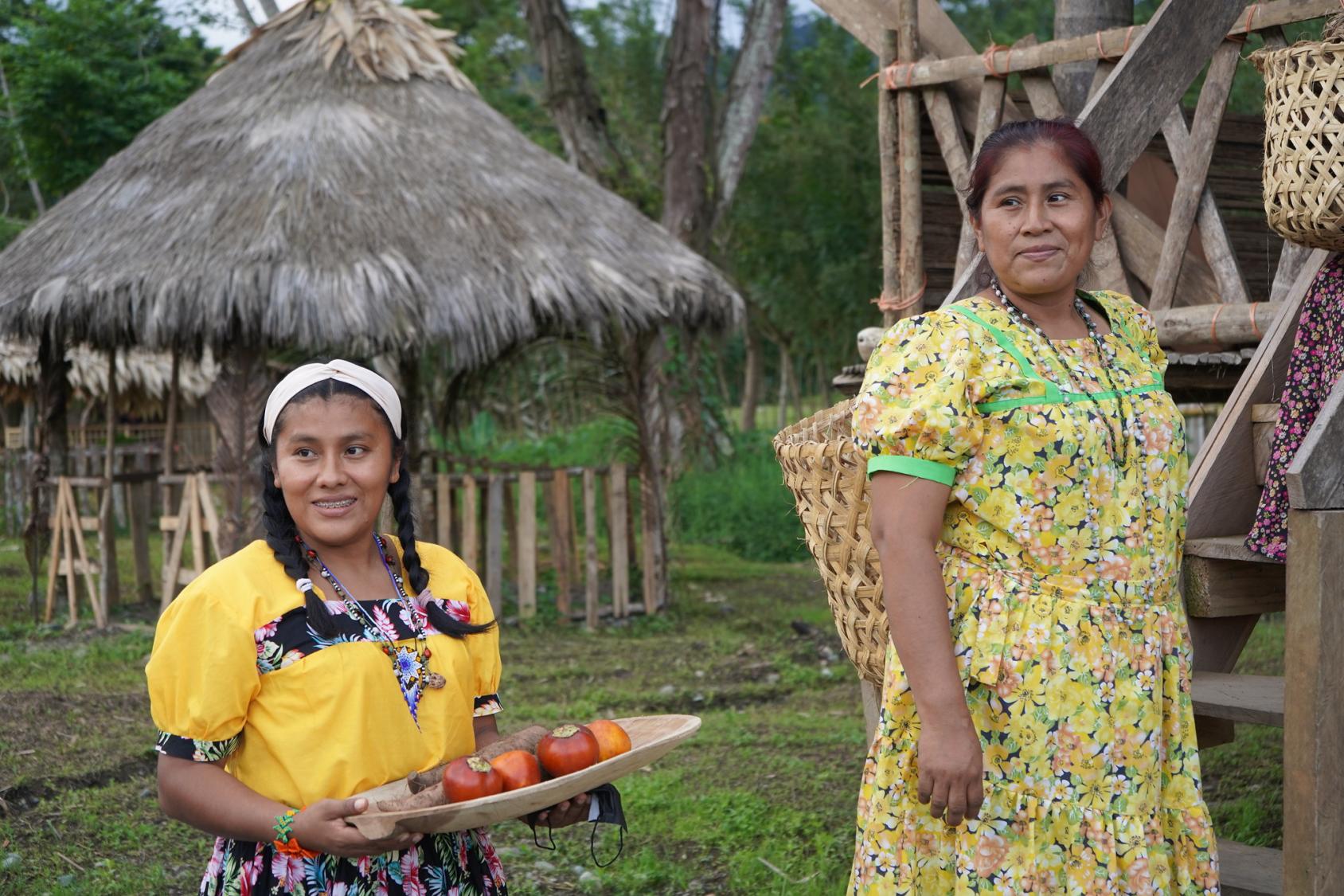 Au Panama, une femme et une jeune fille issues d’une communauté autochtone se tiennent debout devant une hutte, dans leur village, et regardant sur le côté en souriant.