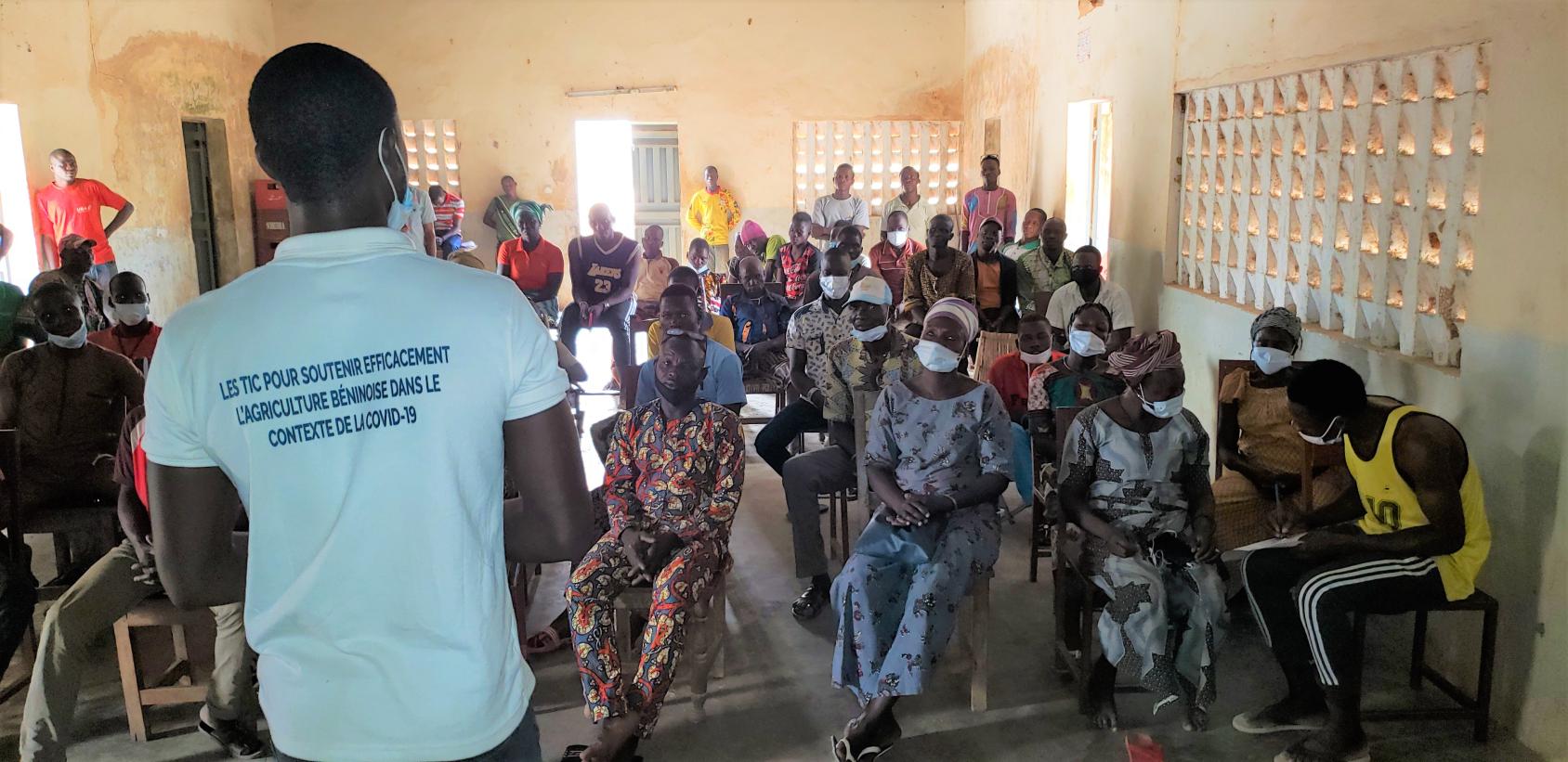Au Bénin, des hommes et des femmes participent à une formation. Ils sont assis dans une salle et écoutent parler un formateur, qui se tient debout devant eux, dos à la caméra.