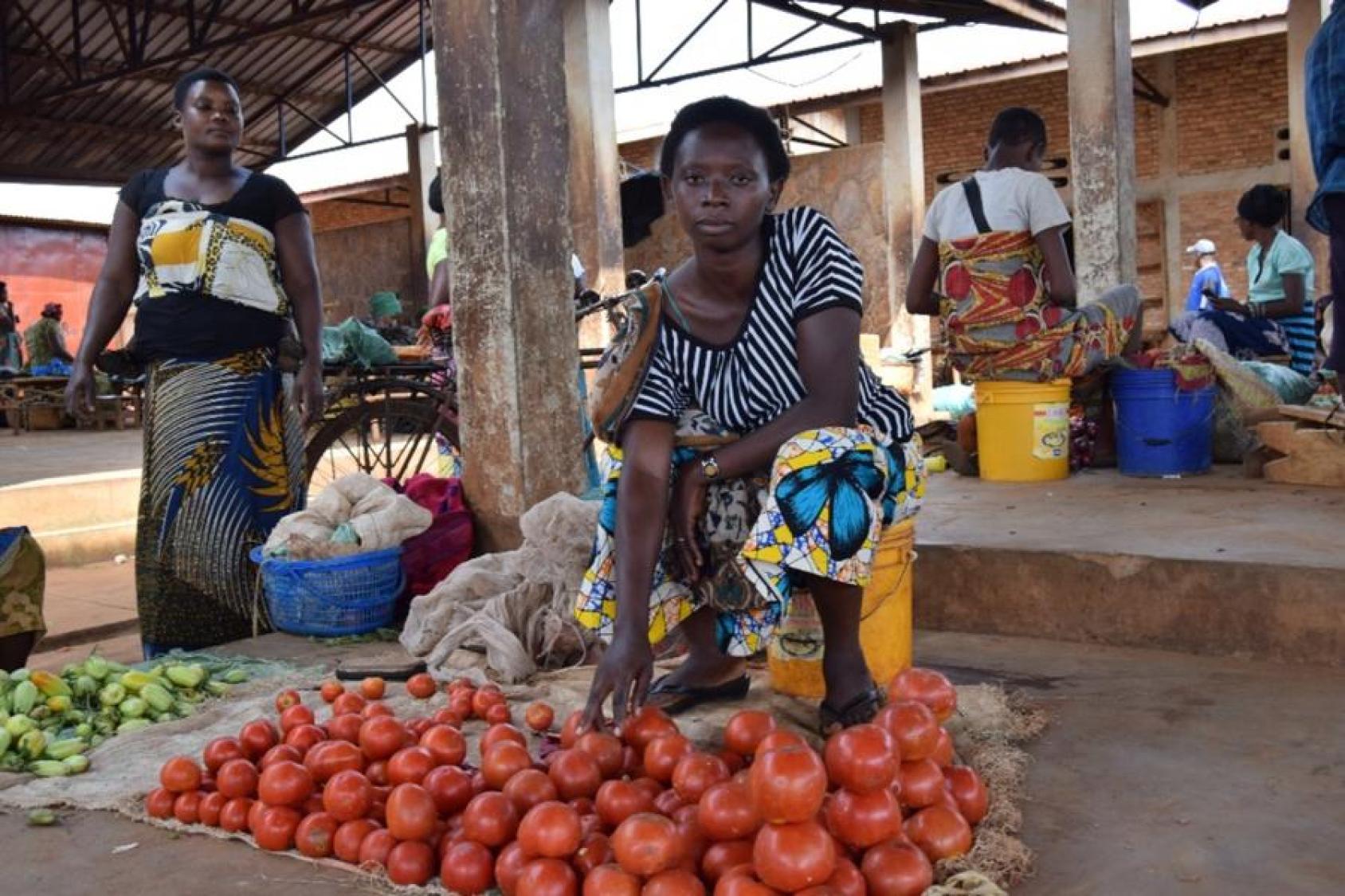 Une femme assise sur un seau vend des tomates dans une halle de marché au Burundi.