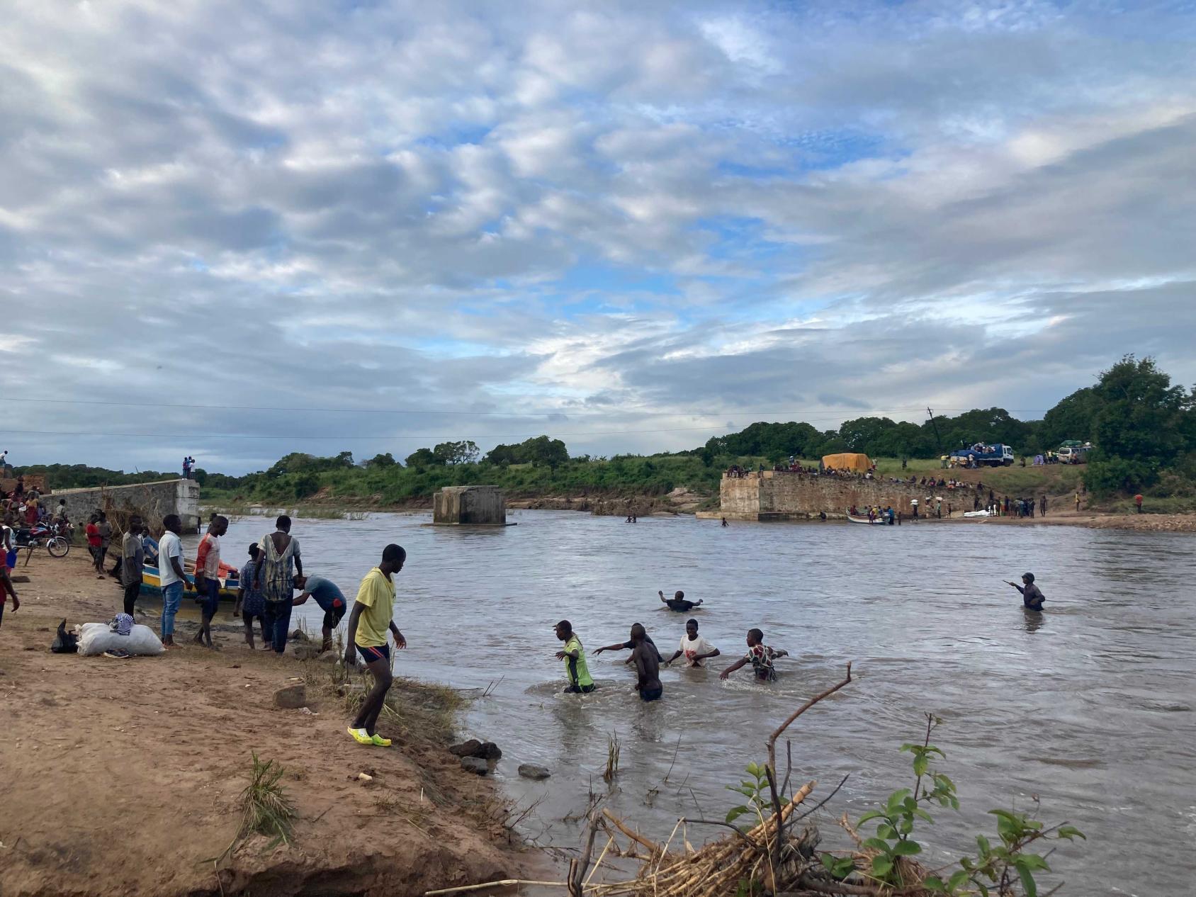 Children play near a river, with a cloudy sky above. 