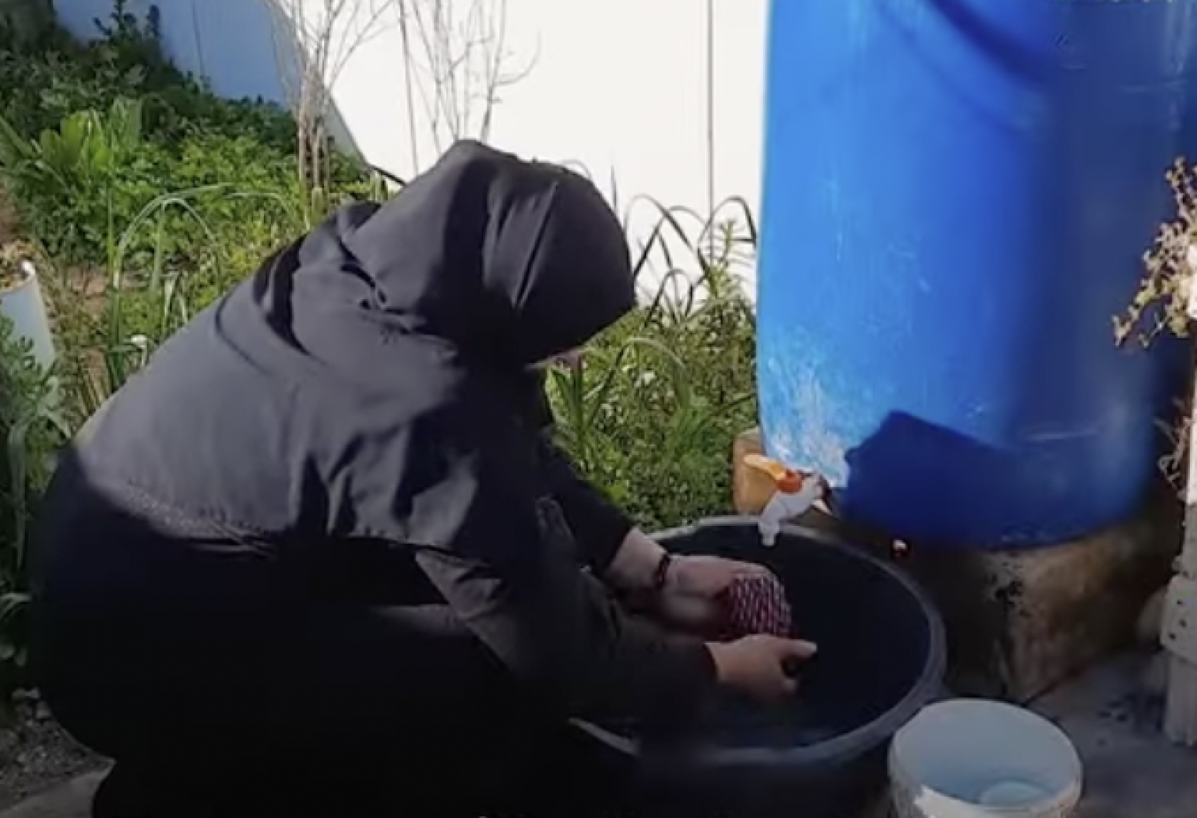 Una mujer utiliza el agua de un tanque de plástico.