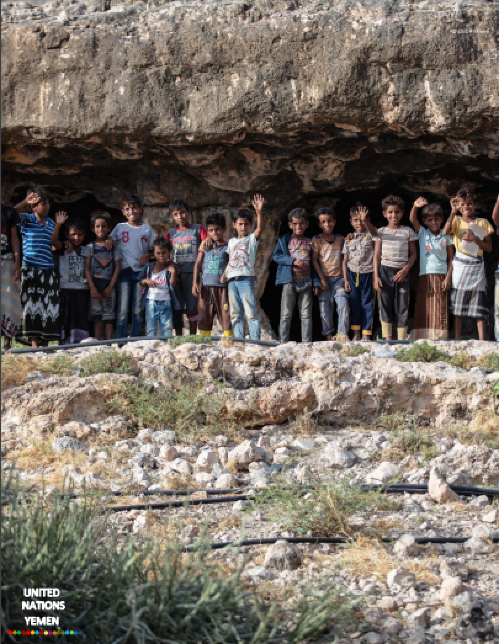 A group of youth-aged boys stand in front of a cave.