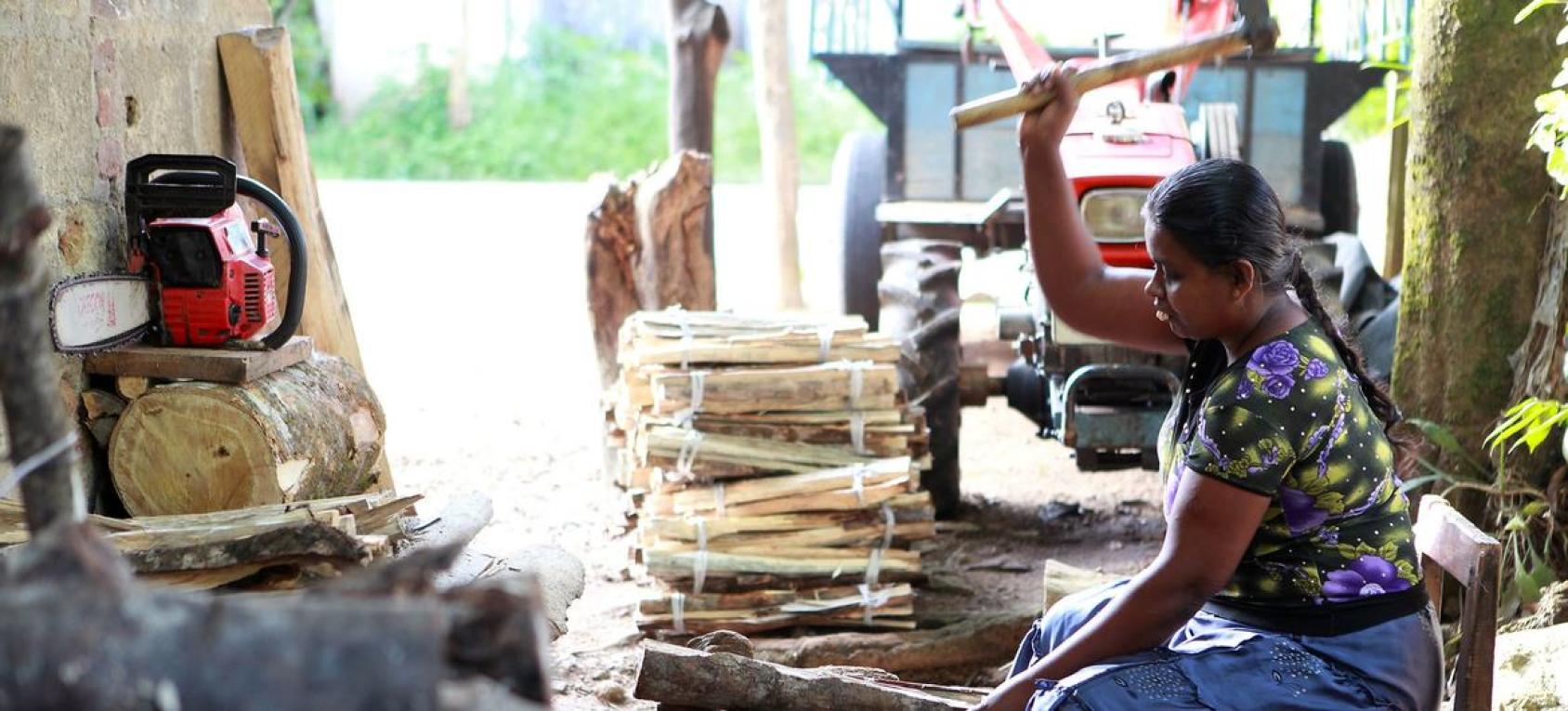 Una mujer se sienta en el suelo y martillea la madera para convertirla en trozos más pequeños.