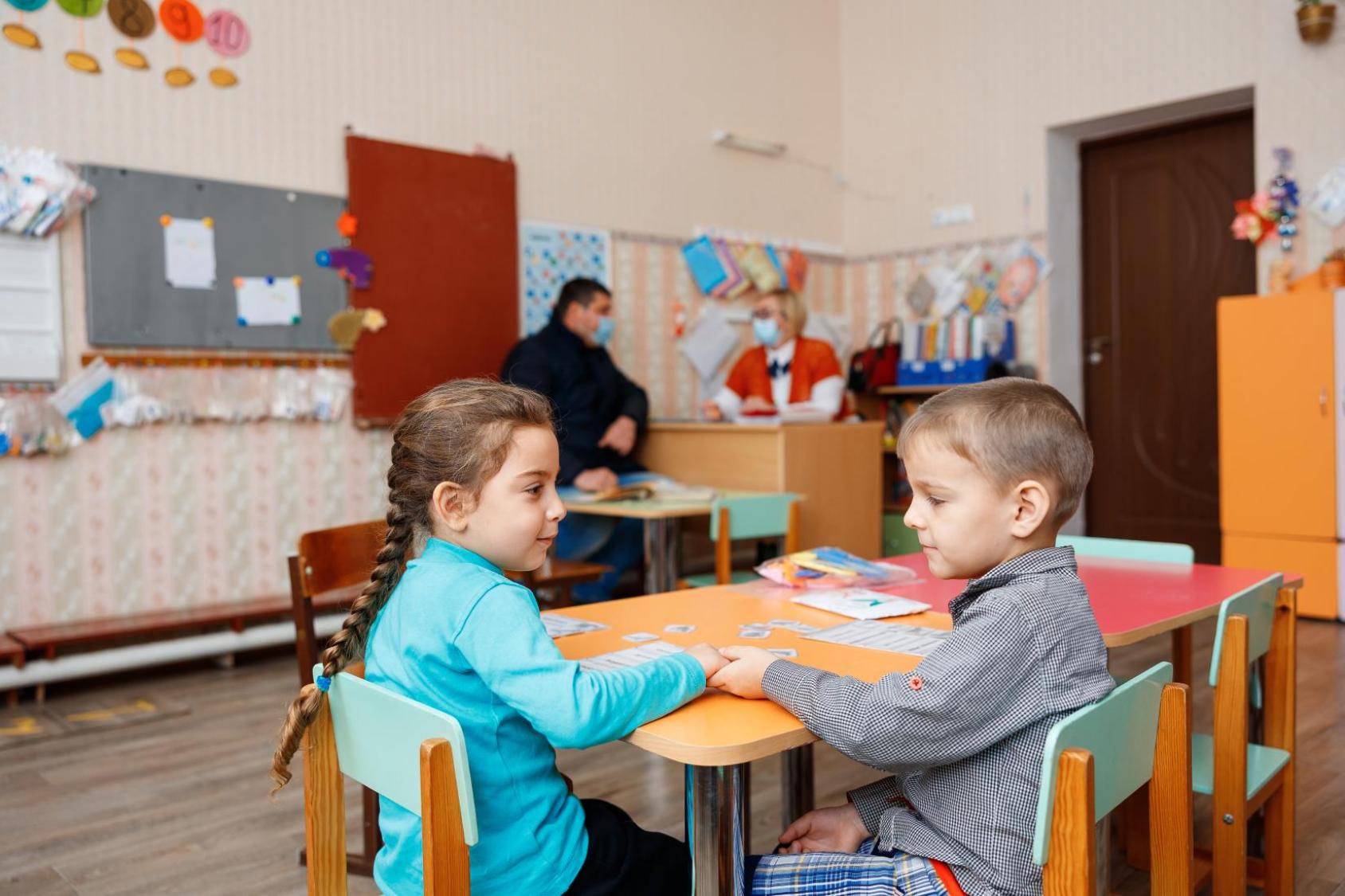 两个小孩子坐在教室里的桌子前。