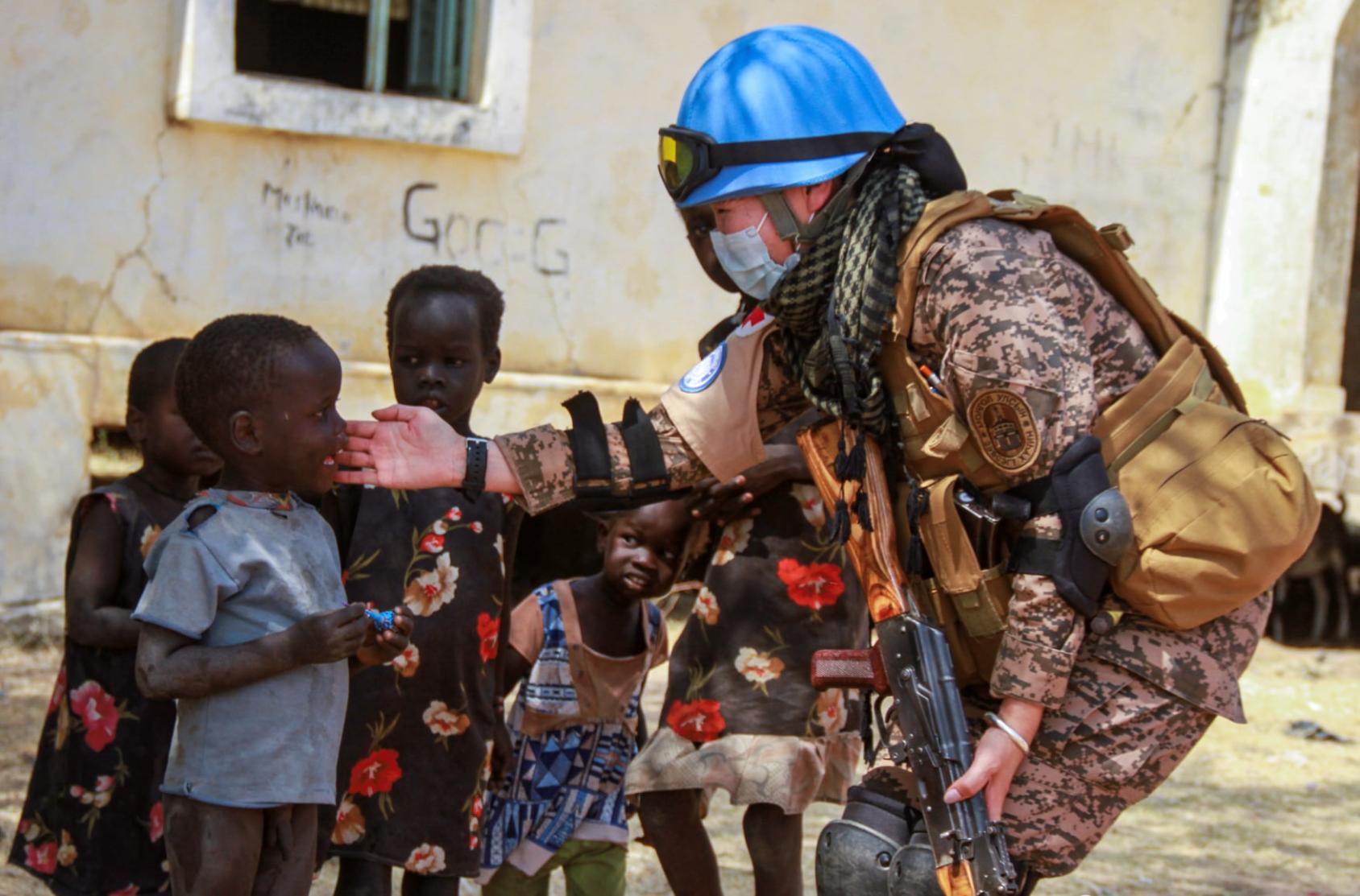 A woman peacekeeper in blue helmet touching the face of a smiling young black boy. 