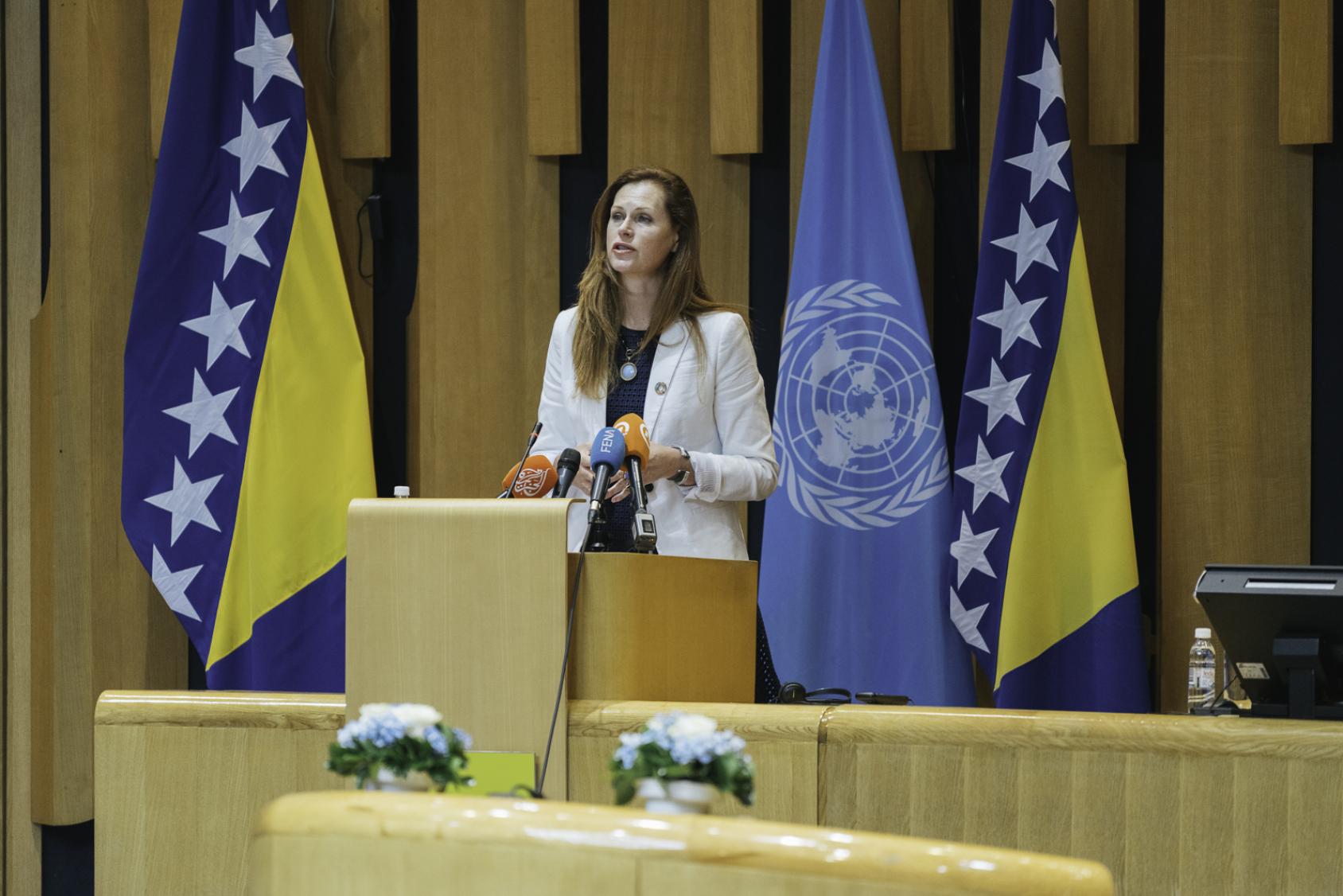 Una mujer con traje beige habla por un micrófono en un podio.