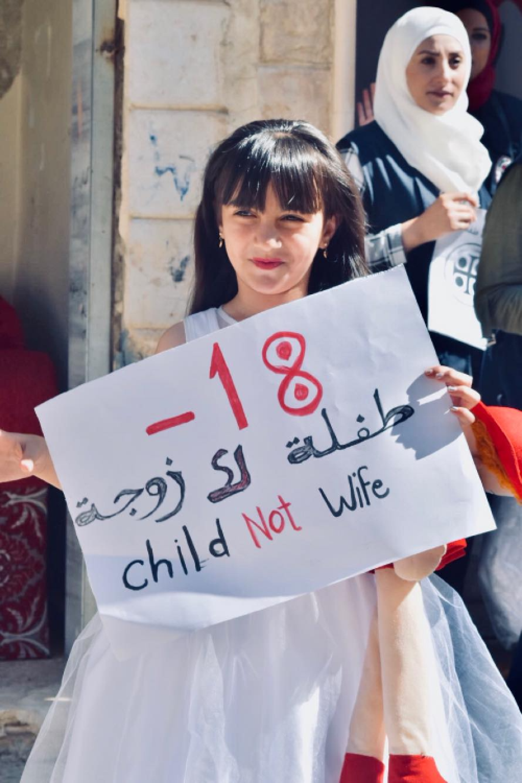 A young girl wearing a wedding dress and holding a sign that says: child not wife.