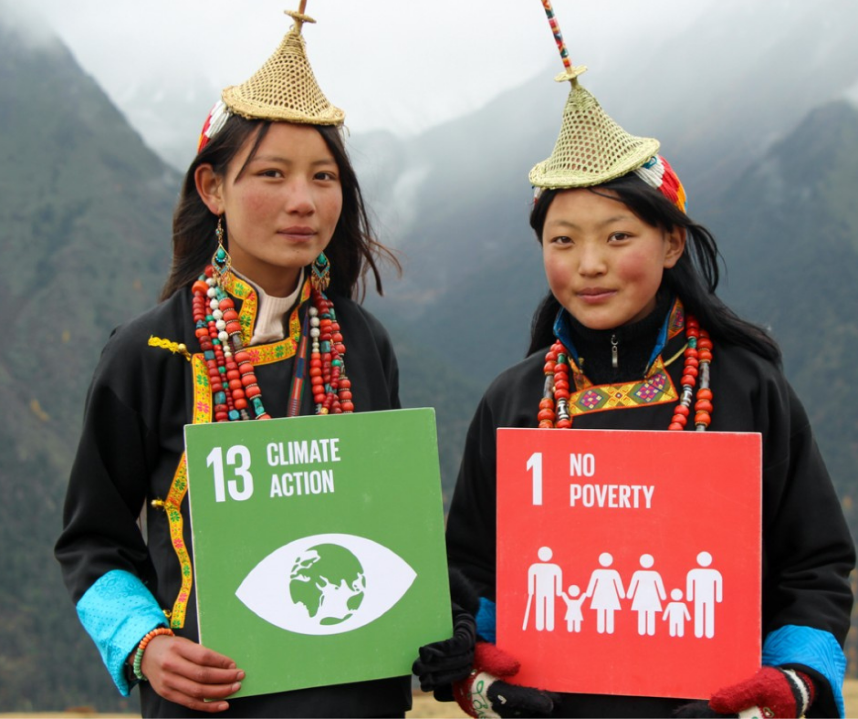 Con montañas y nubes como fondo, primer plano de dos jóvenes de Bhután con carteles de los ODS13 y ODS1.