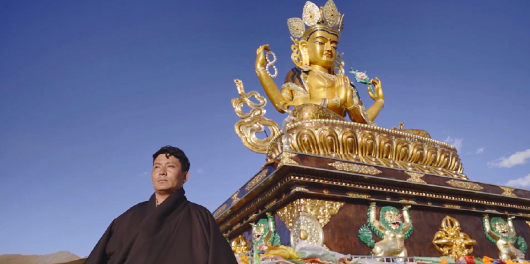 Un homme se tient devant un stoupa (structure architecturale bouddhiste) tibétaine, par une belle journée ensoleillée.