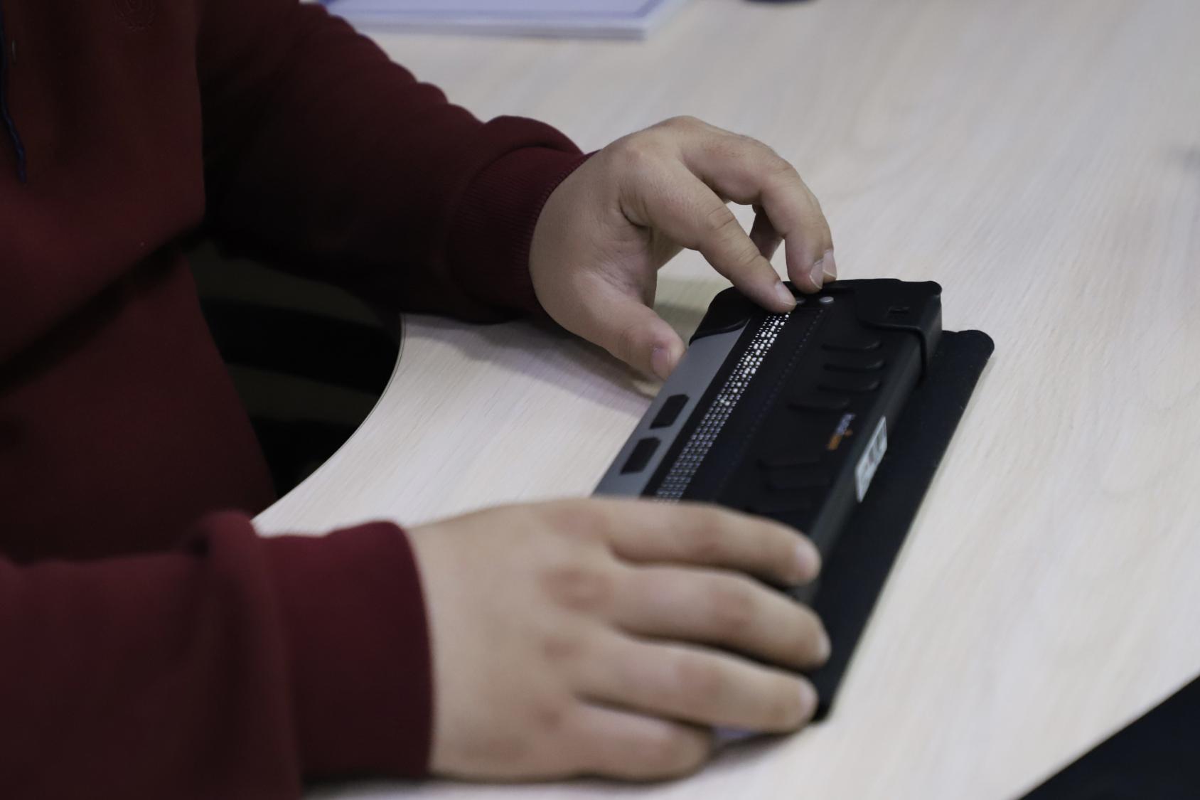 Hands of a person in a red shirt holding a Braille reading instrument