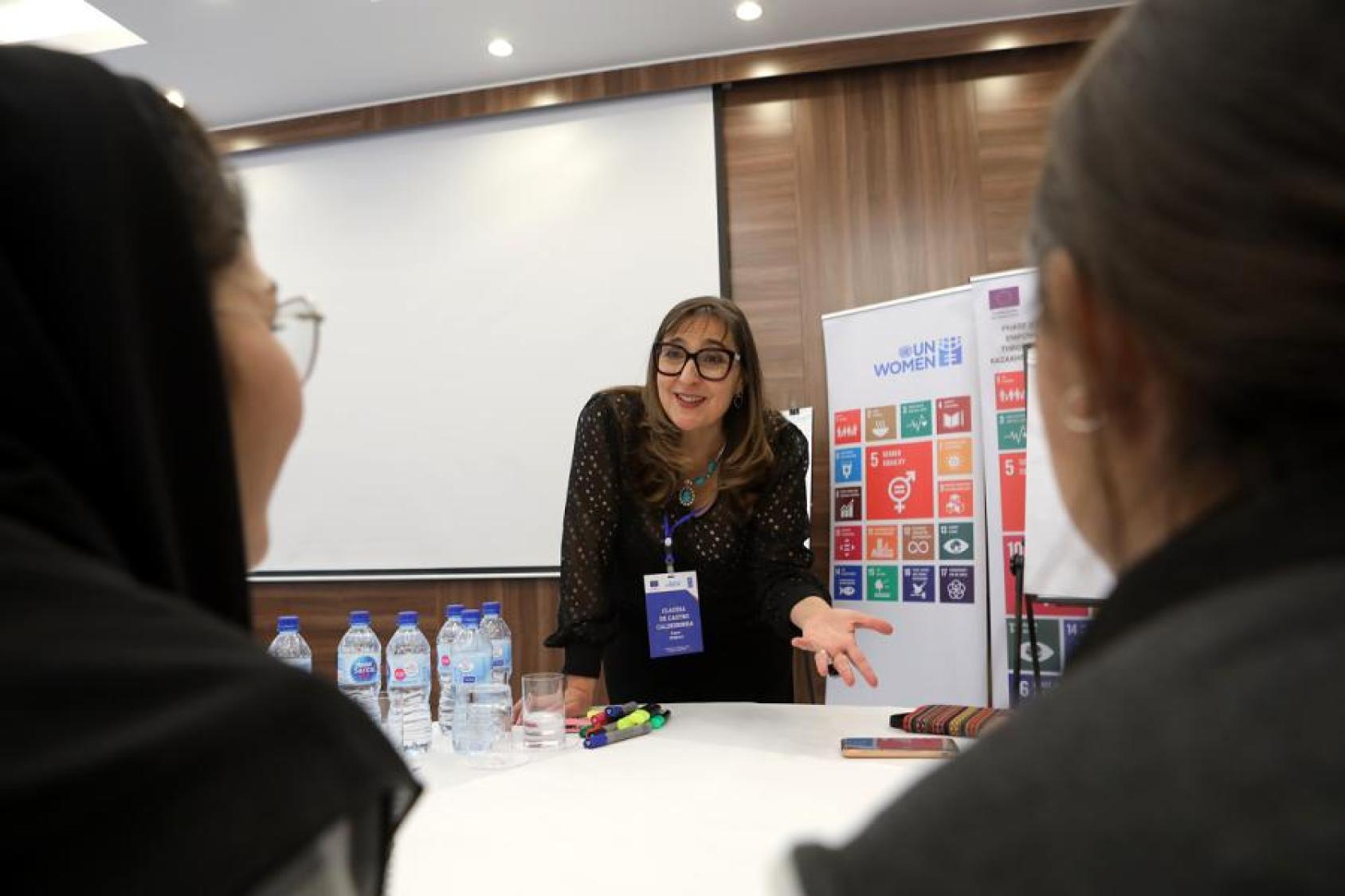 A female trainer discusses something with participants with the SDGs behind her.