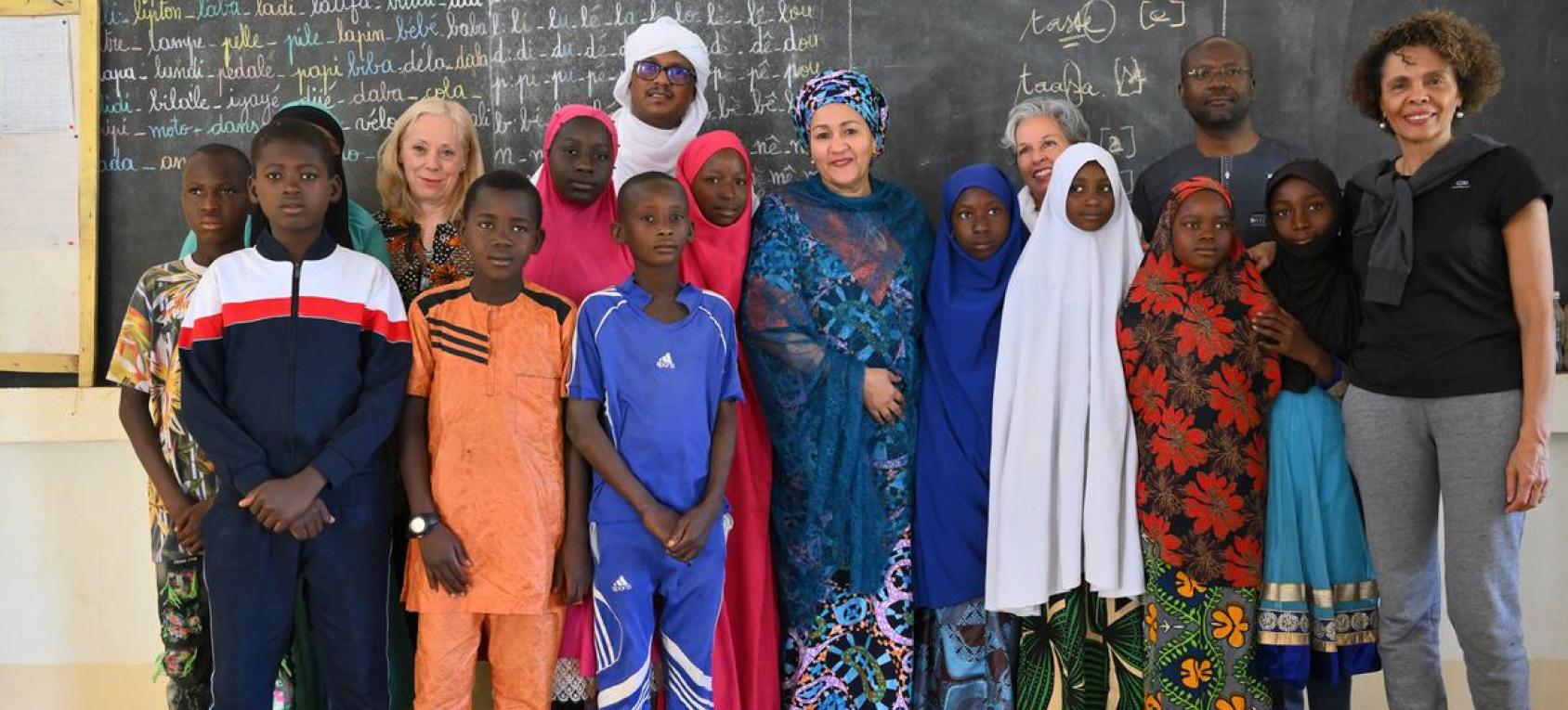 Schoolchildren standing in front of a blackboard with UN DSG Amina Mohammed