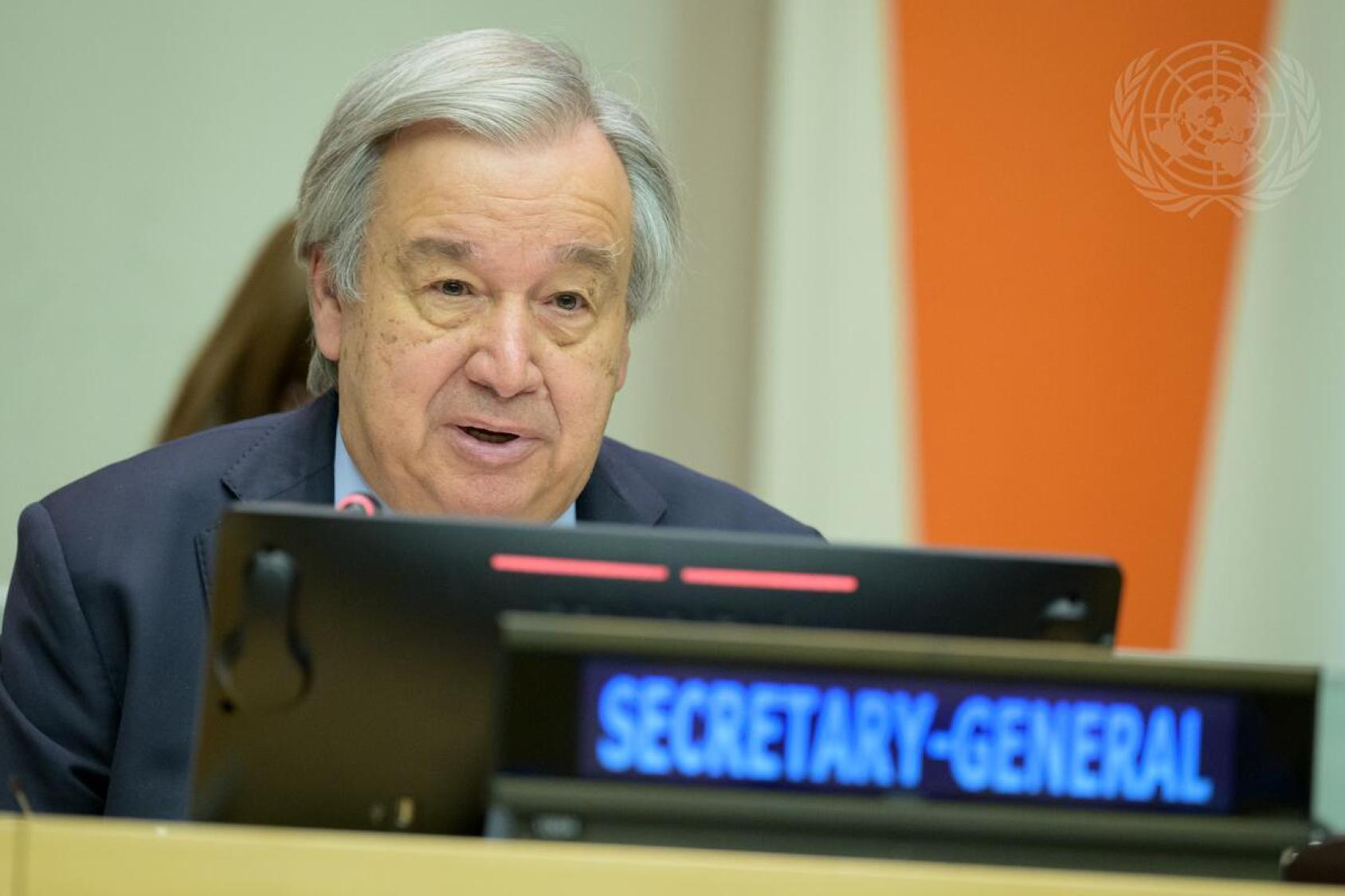 The UN secretary general sits at a podium and speaks into a microphone