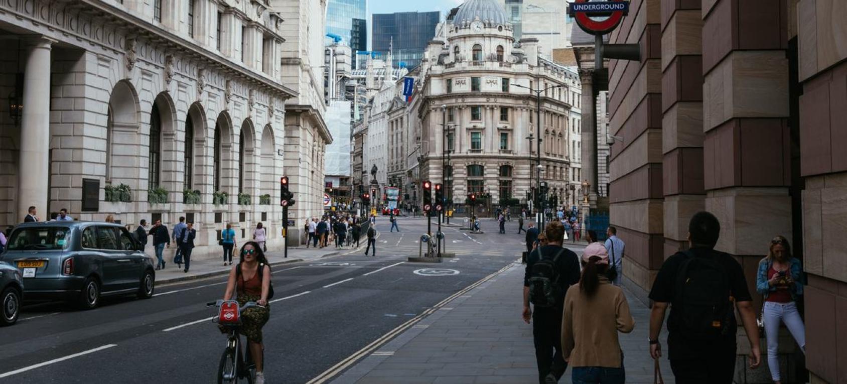 An intersection in London with old bank buildings in the background and people crossing the street in the foreground