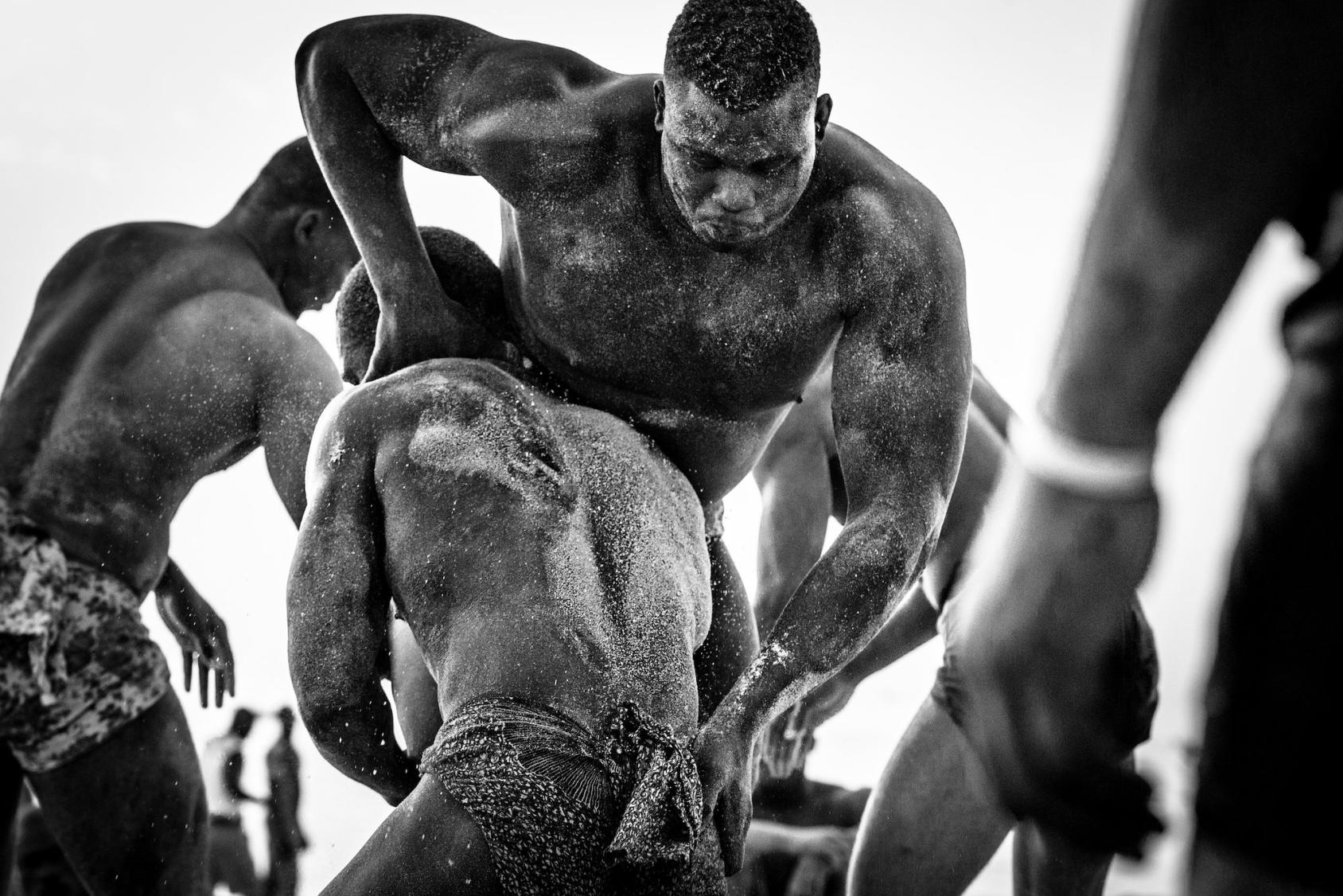 A black and white photo of two African men wrestling in the sand