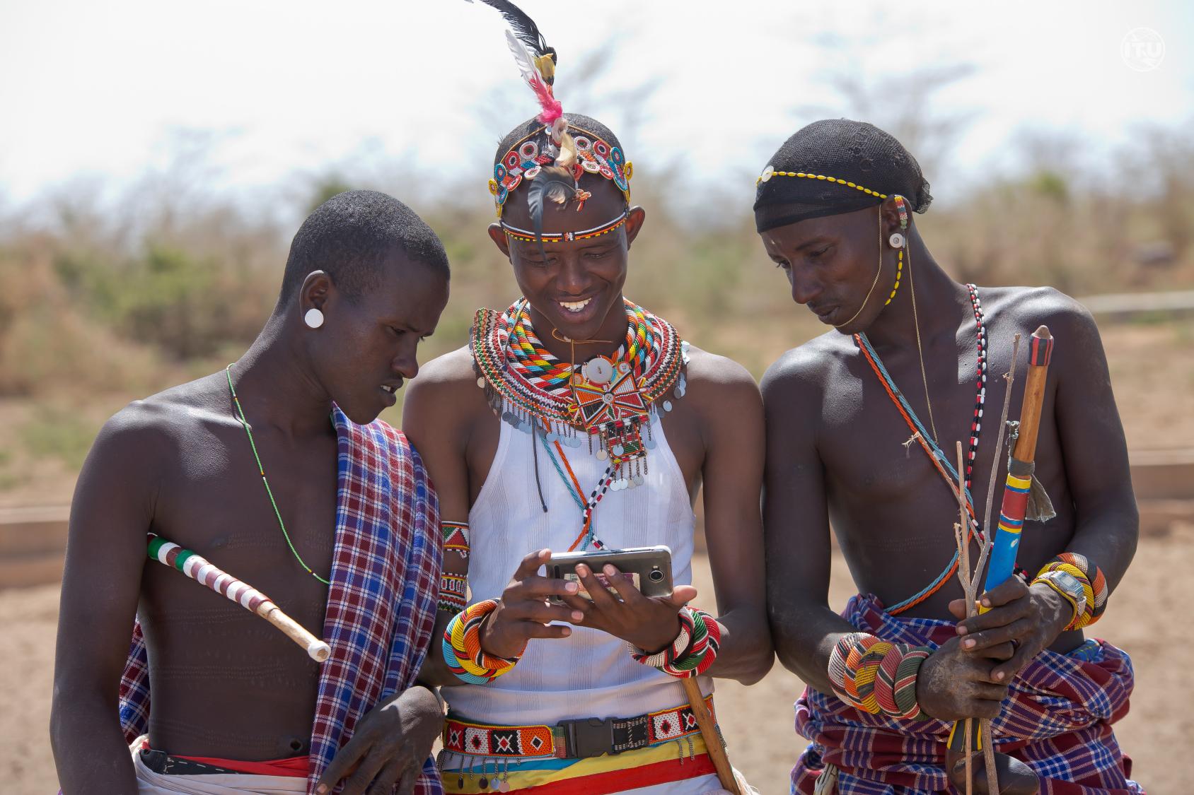 Three men in tribal attire peep into a mobile phone in Kenya