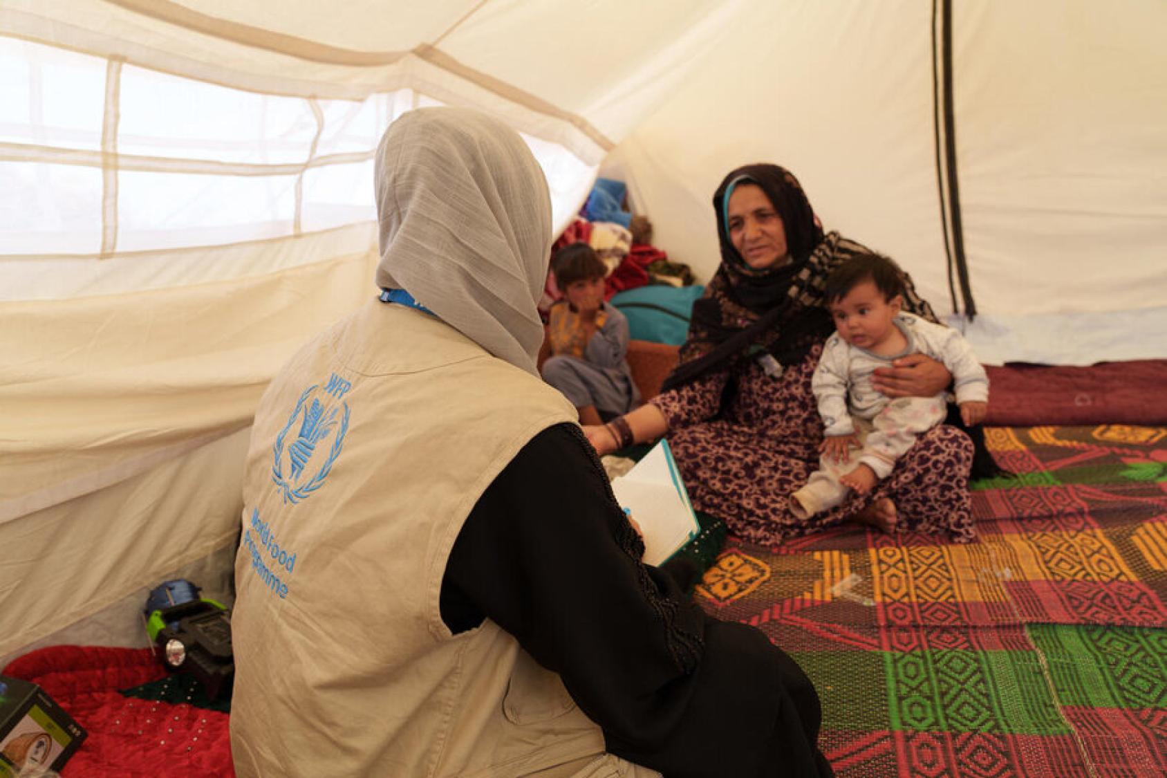 A WFP food monitor speaks to a grandmother holding a baby in a tent in Afghanistan