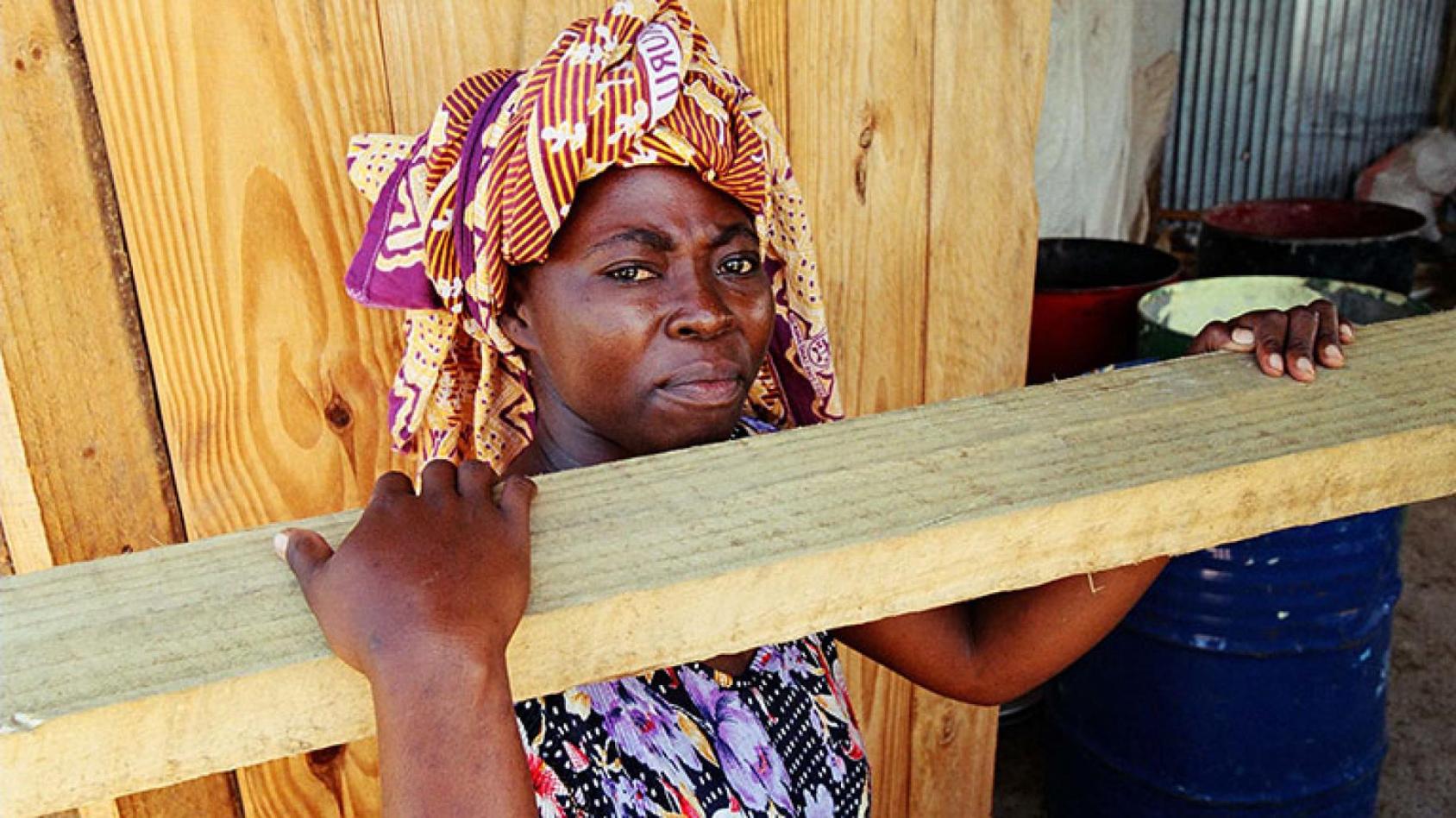 A woman with a scarf carries a plank of wood 