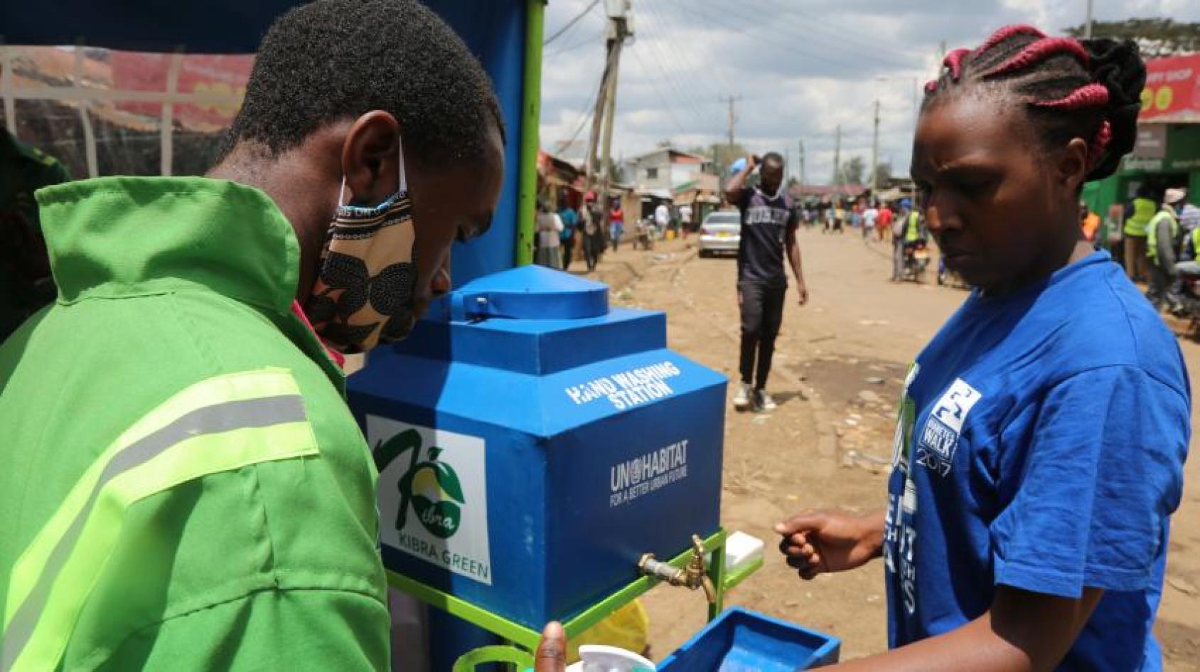 A woman in a blue shirt and a man in a green one fill water from a public tap in Kibera, Nairobi
