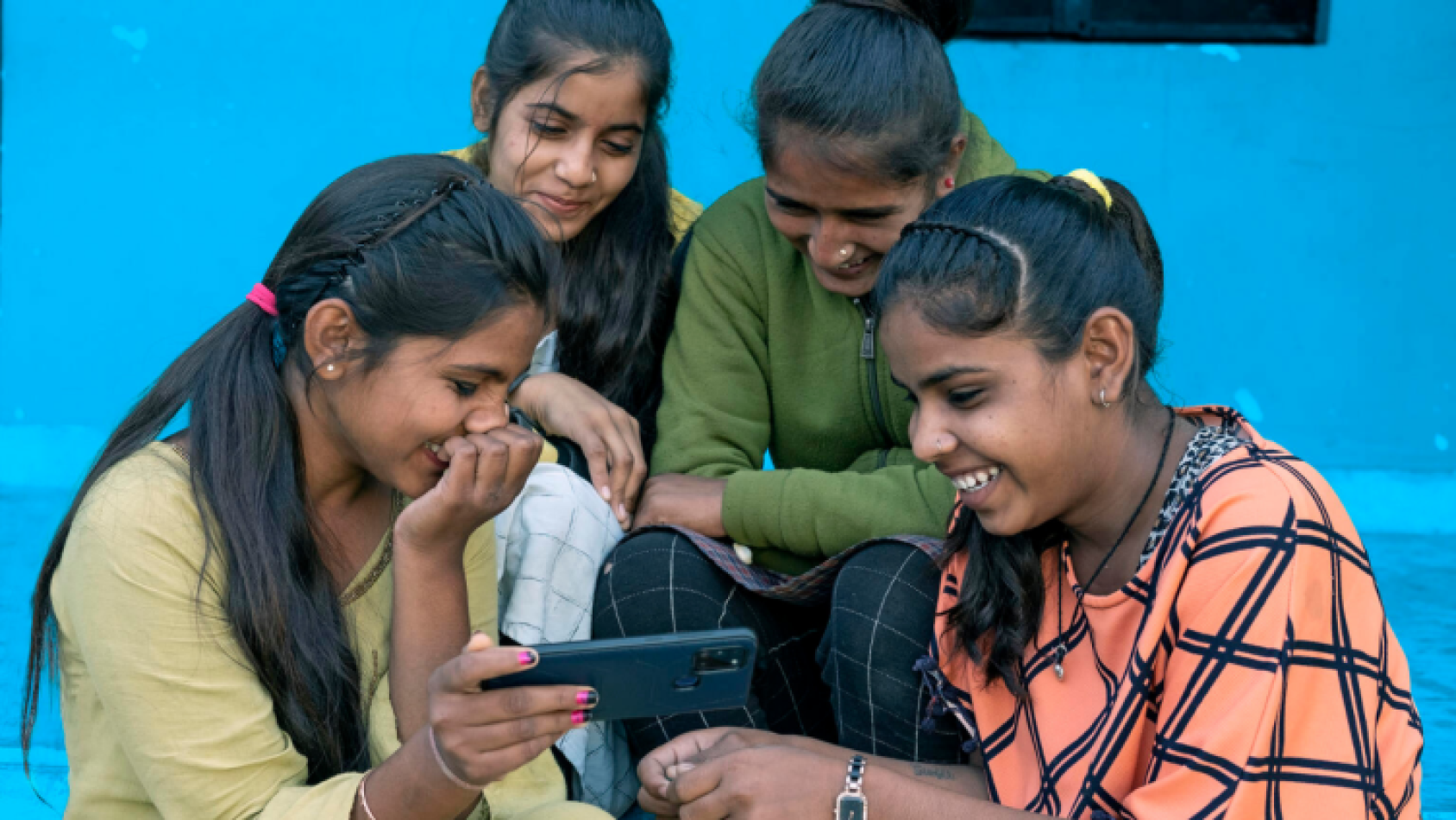 Four girls crowd around a mobile phone giggling