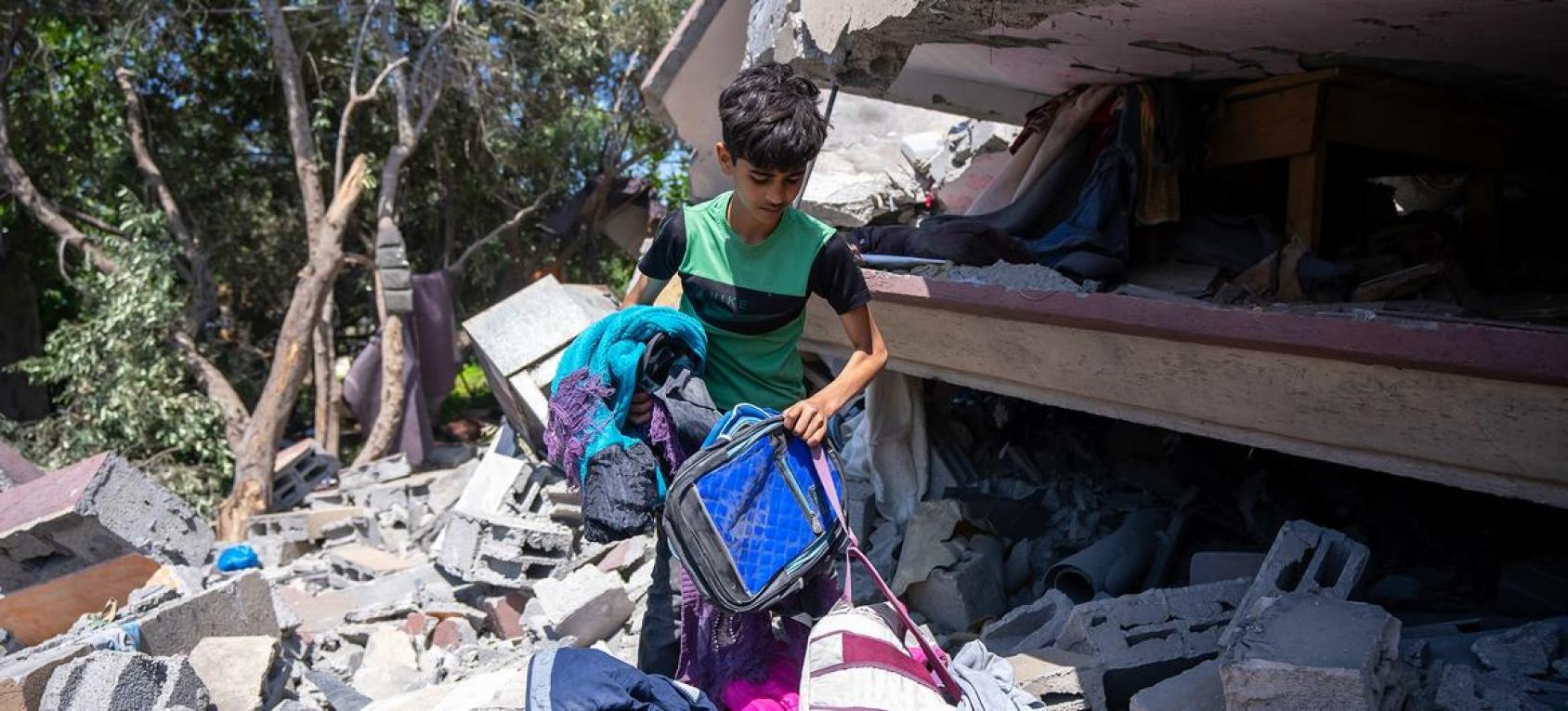 一名学龄男孩在瓦砾和被毁坏的建筑物中搬运物品。
