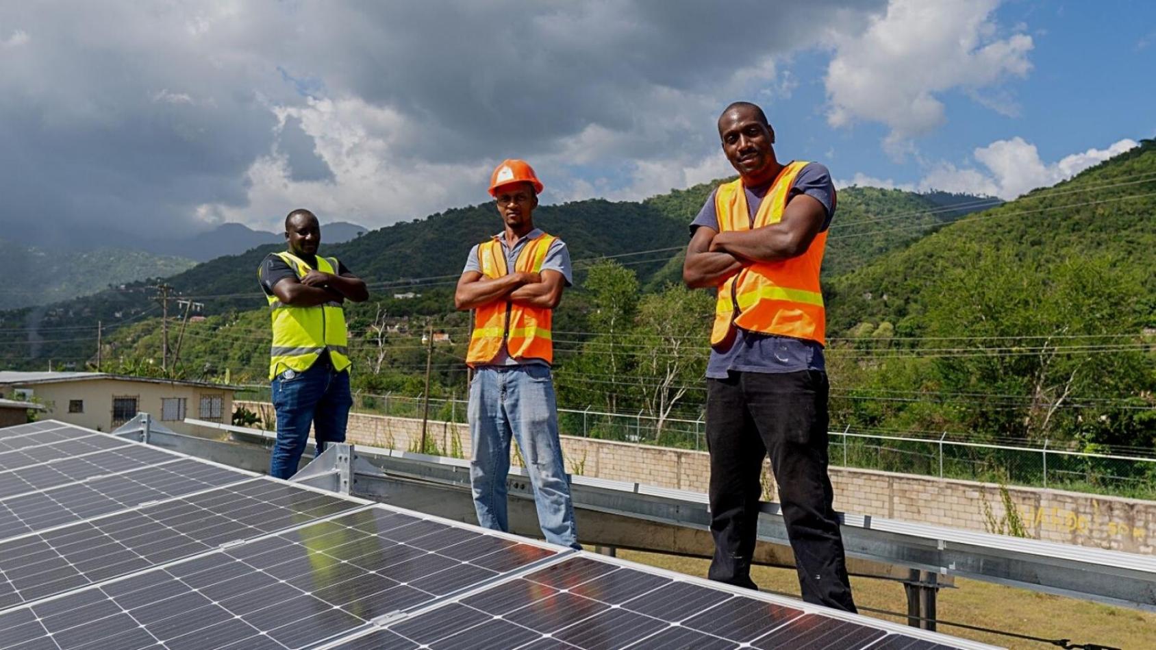 Three men in uniform standing in front of a solar panel in Jamaica