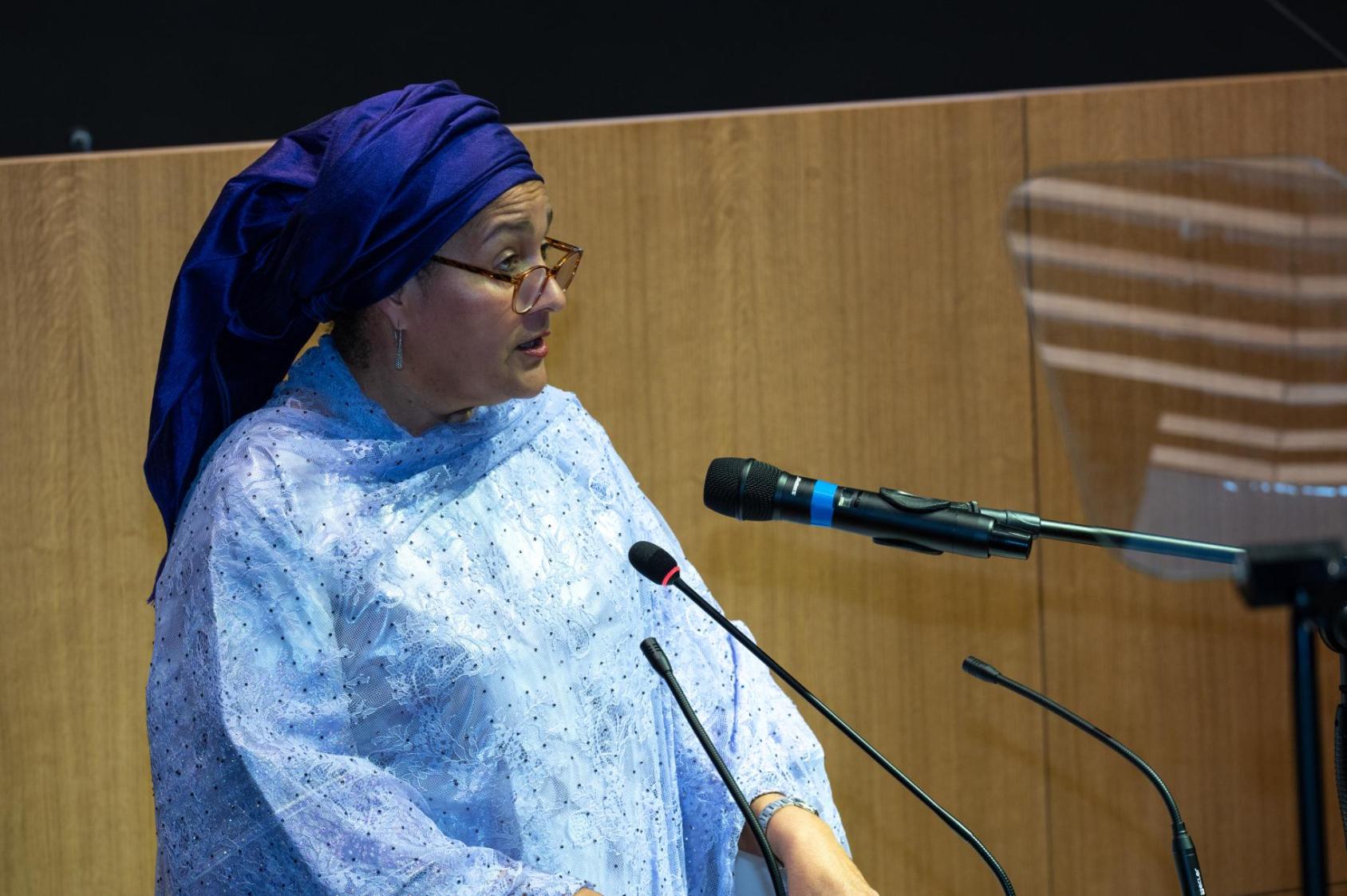A woman in a light blue dress and dark blue hair turban, the UN Deputy Chief Amina Mohammed, speaks into a microphone at the UN House in Senegal