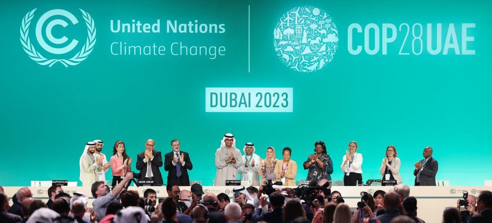 A group of 11 people stand on a podium with a green back-ground signifying the UN Climate Change Conference COP28 in Dubai.