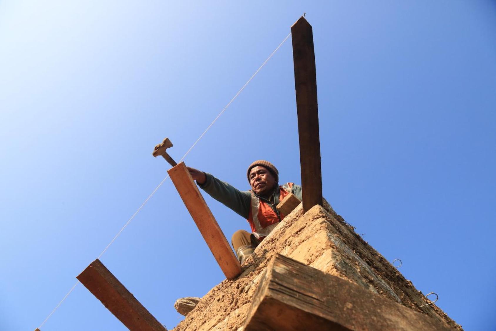 A woman with a hammer peers over the scaffolding of a building in Nepal
