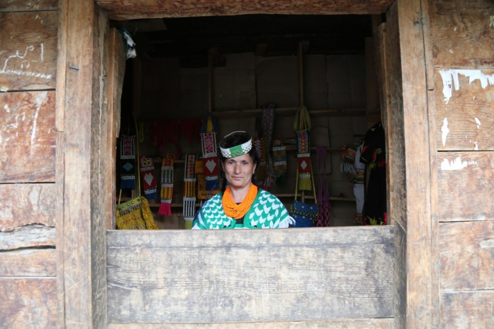Женщина в окне деревянного дома, одетая в народный костюм калаши в Пакистане