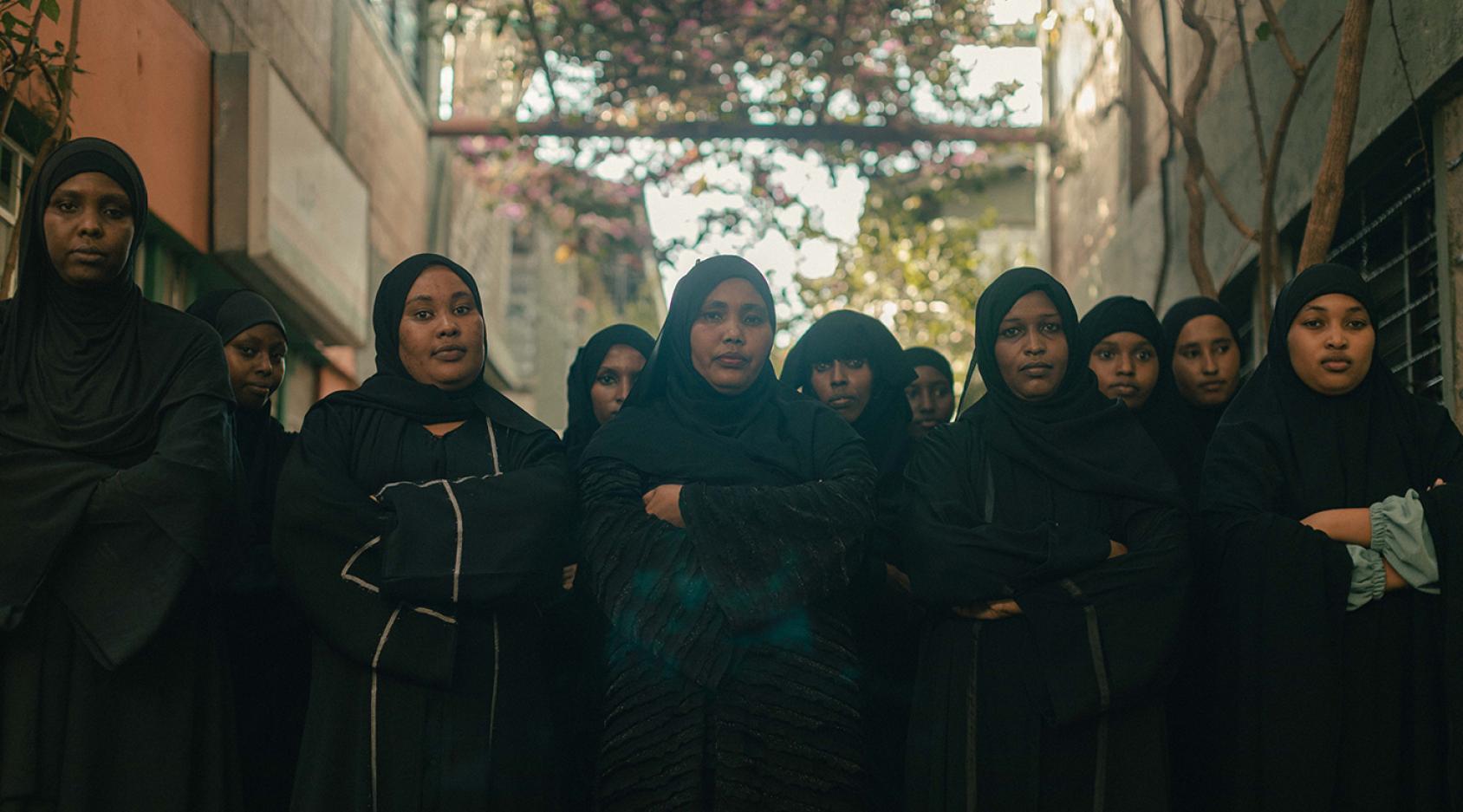 A group of women in black full length abaya clothes standing next to each other.
