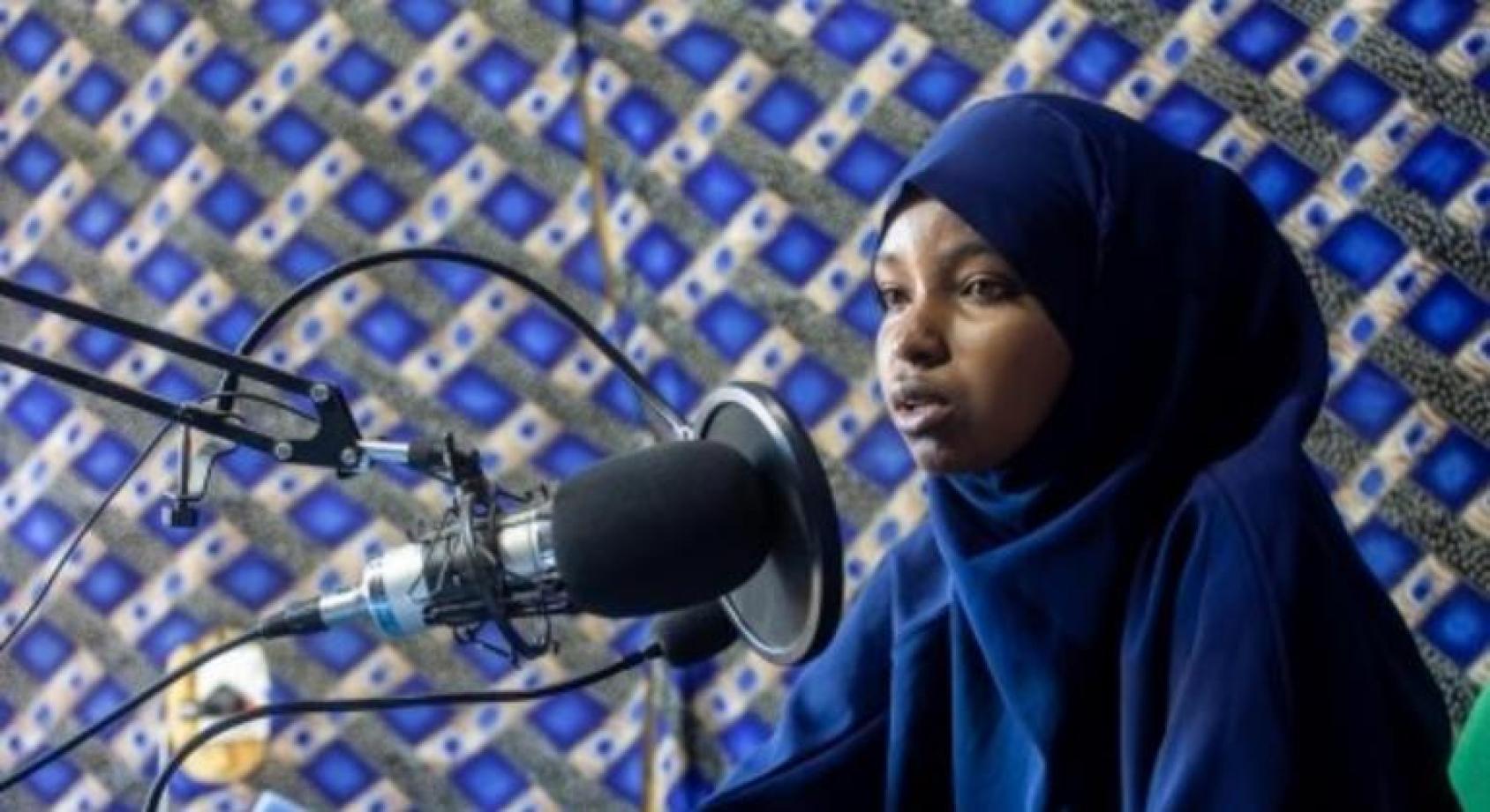Сомалийка сидит перед профессиональным радио микрофоном и о чем-то рассказывает