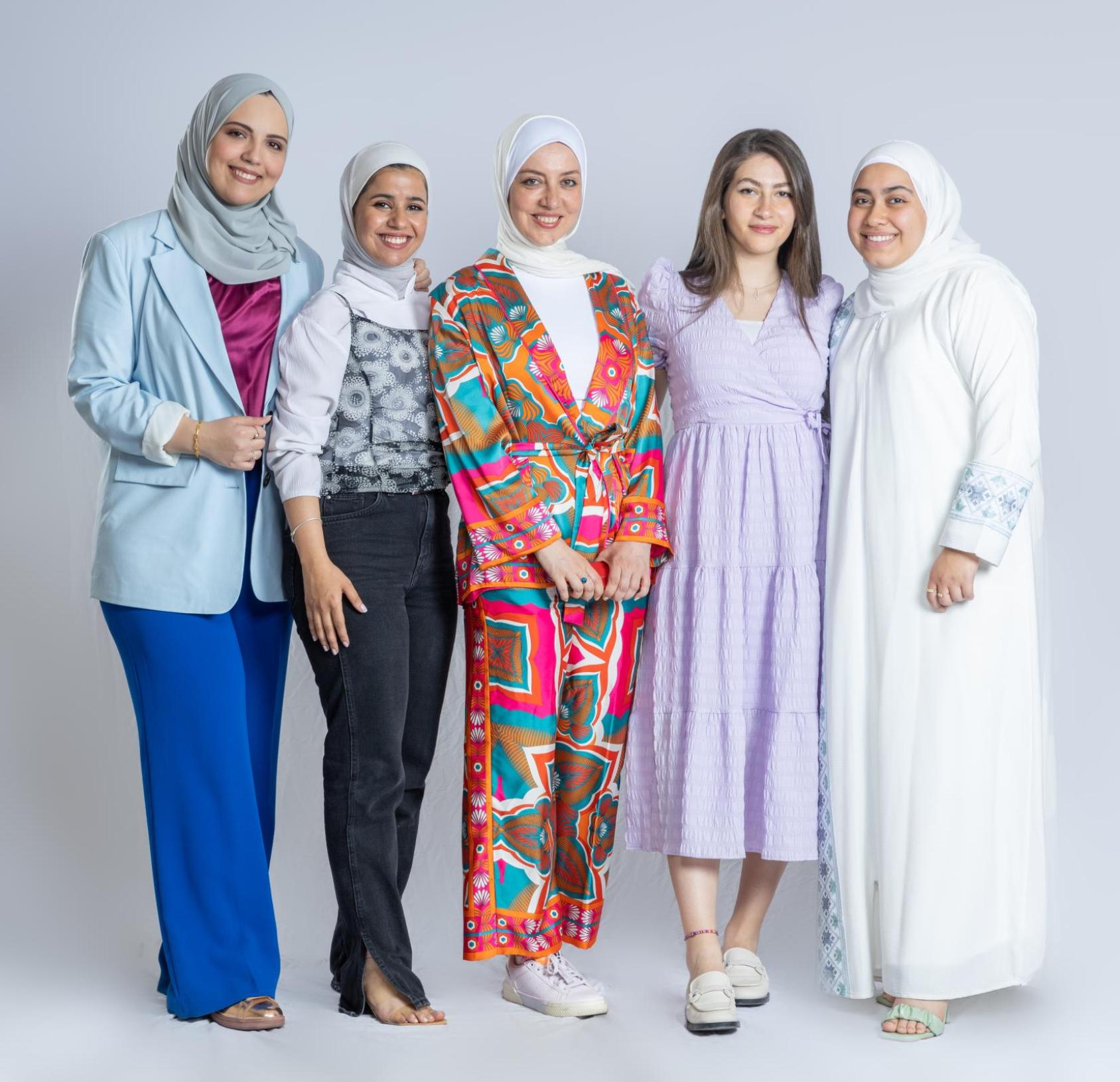 A group of five women in colourful clothes and headscarves stand next to each other smiling.