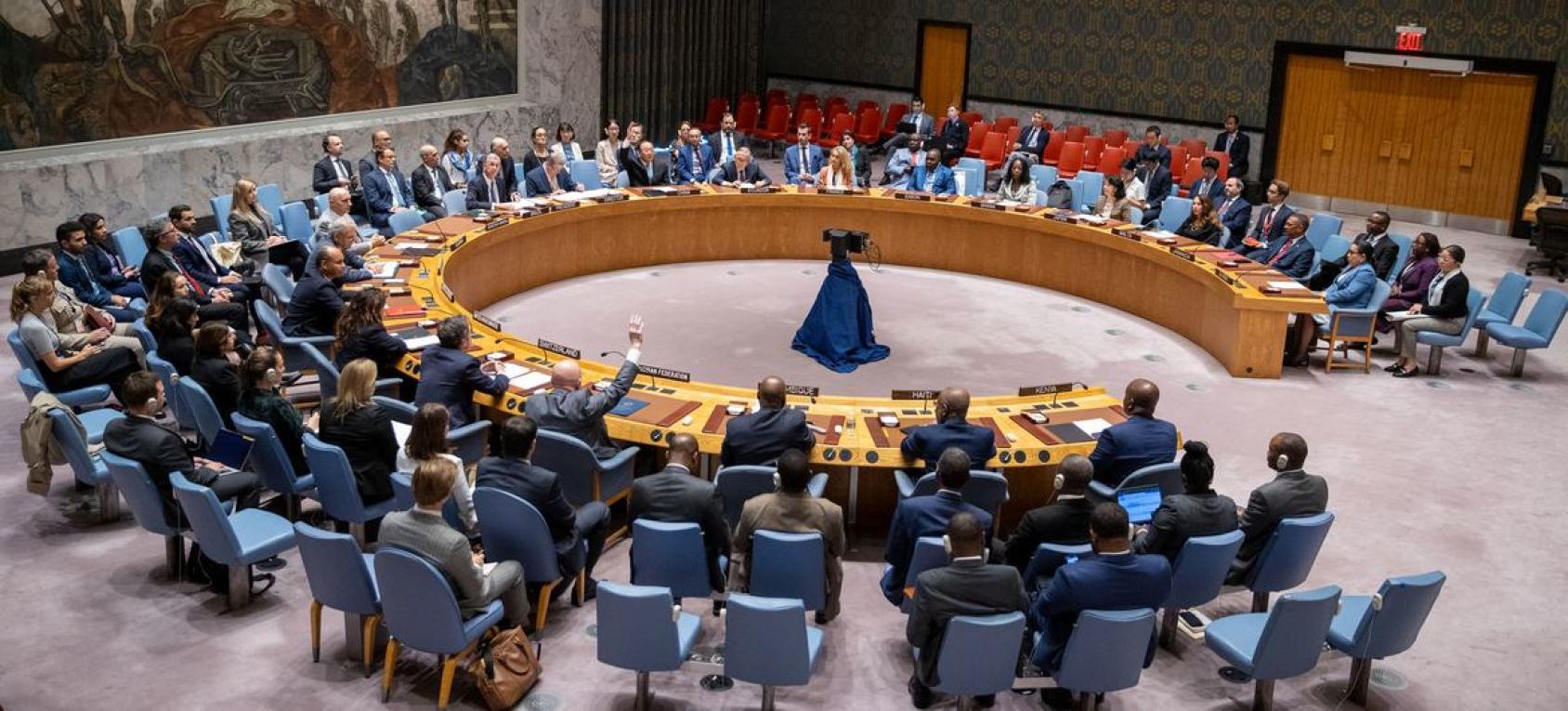 A circular table depicting the UN Security Council around which numerous people in suits are sitting and talking.