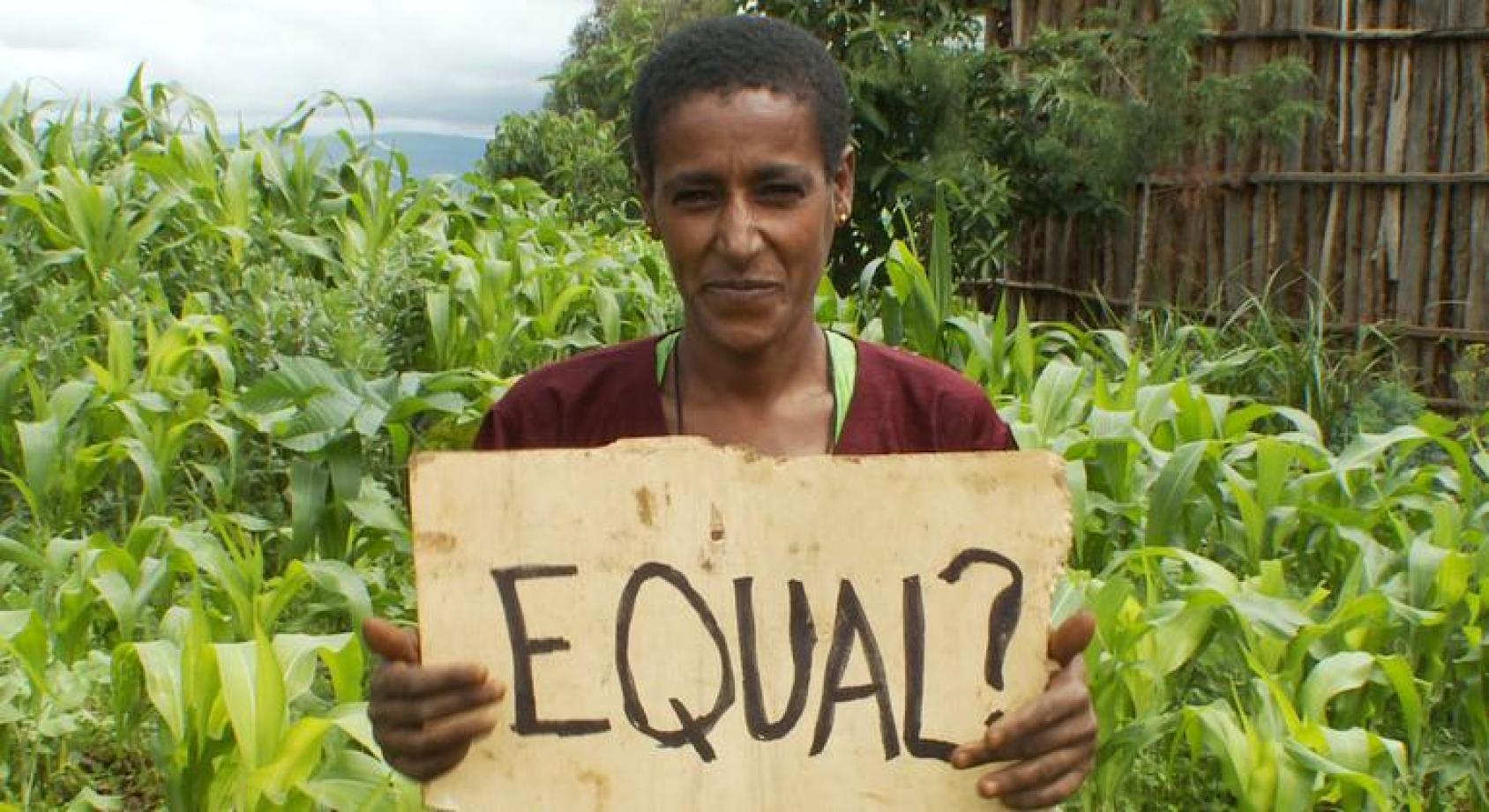 Женщина на фоне плантации с табличкой в руках " Равные?"