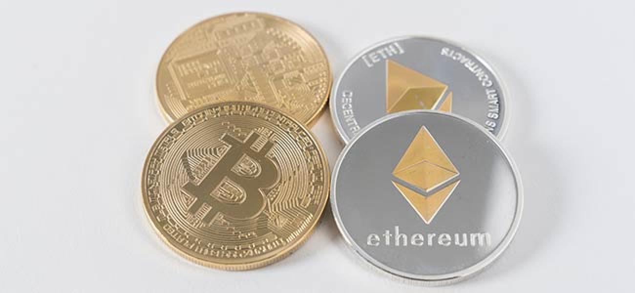 Photographie montrant quatre pièces rondes ressemblant à des pièces de monnaie, deux portant le symbole du Bitcoin et les deux autres celui de l'Ether.